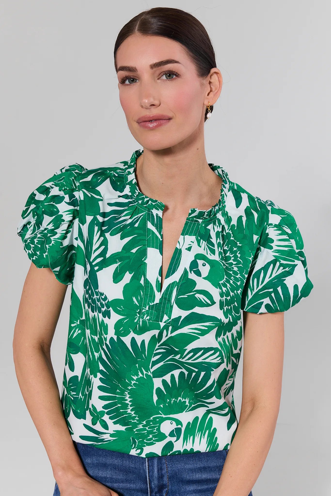 Woman wearing a green and white leaf-patterned blouse against a gray background