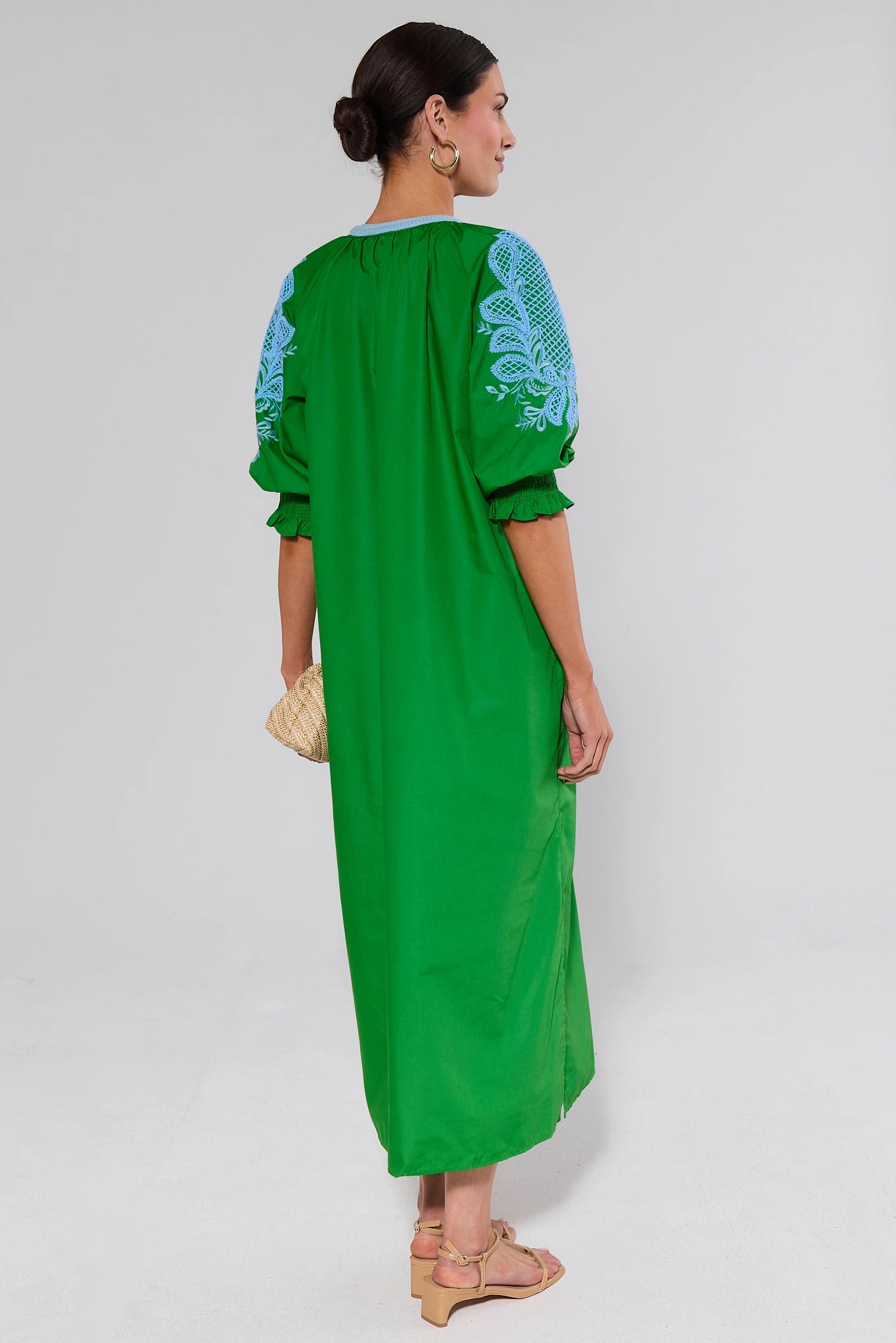 Woman standing wearing a green dress with blue embroidery on a white background