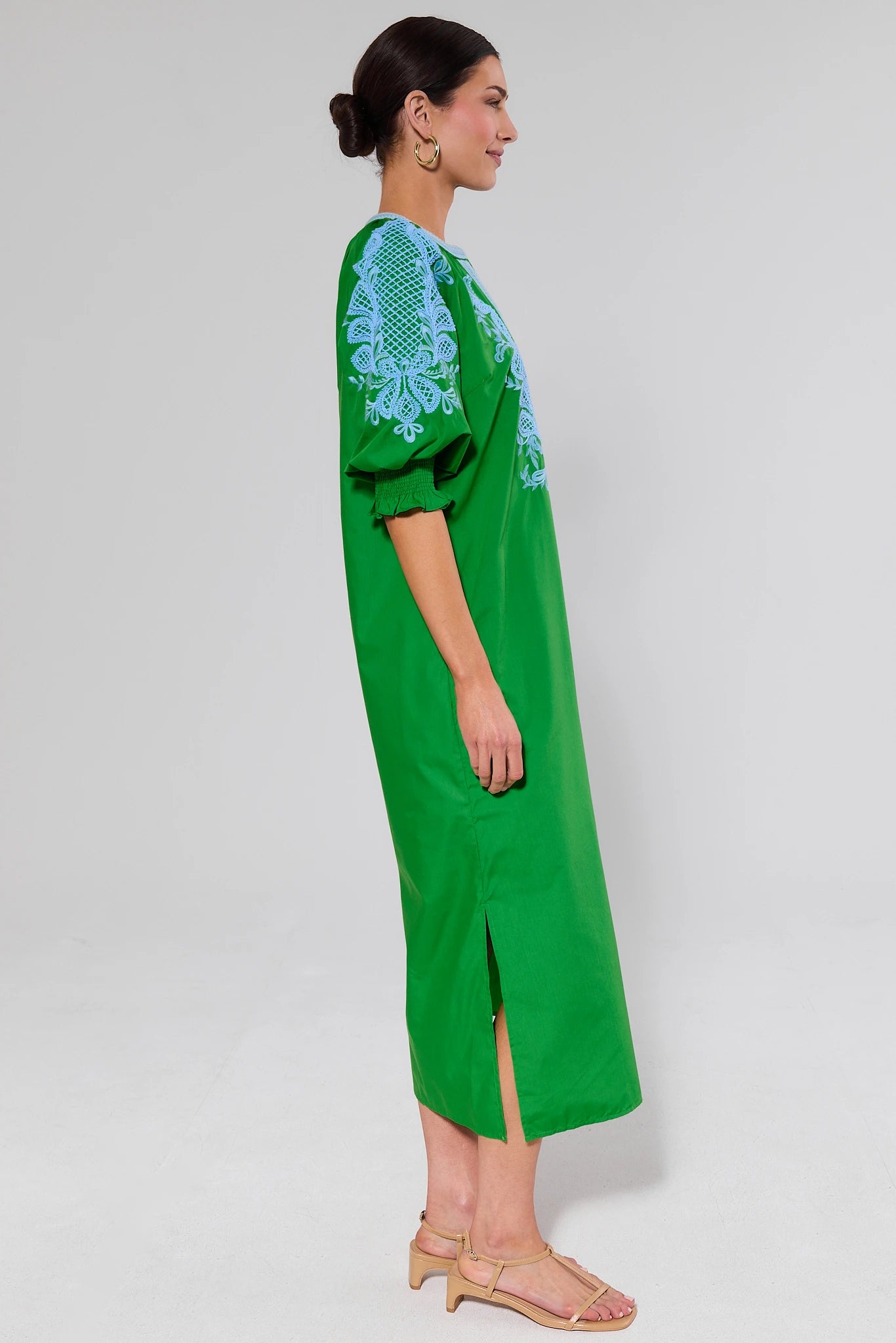 side shot Woman wearing a green dress with blue embroidery on a white background