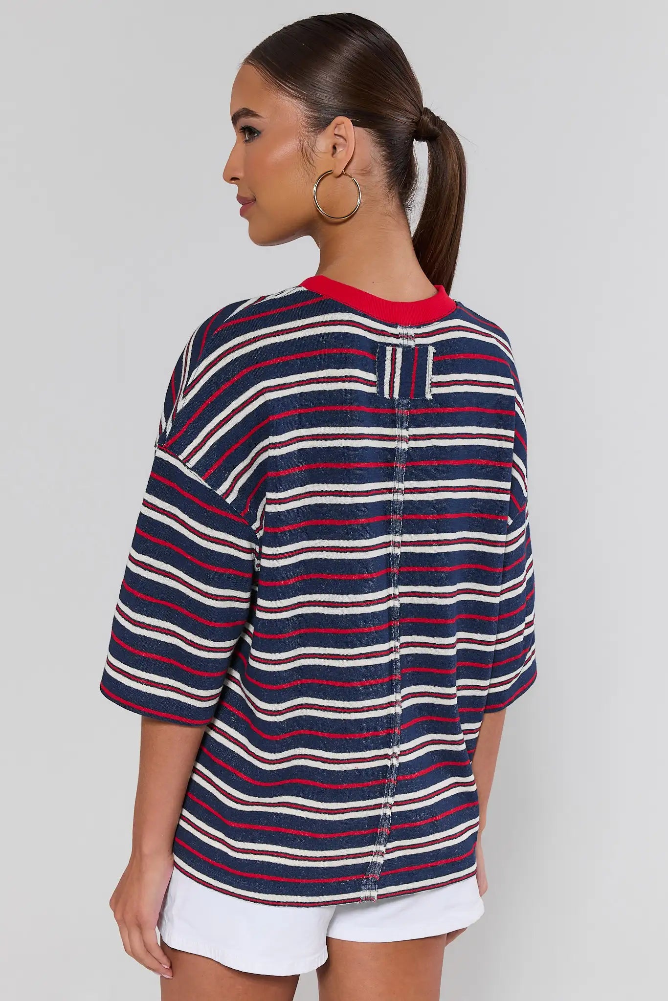 Woman standing wearing a striped shirt with red, white, and blue horizontal stripes on a plain background