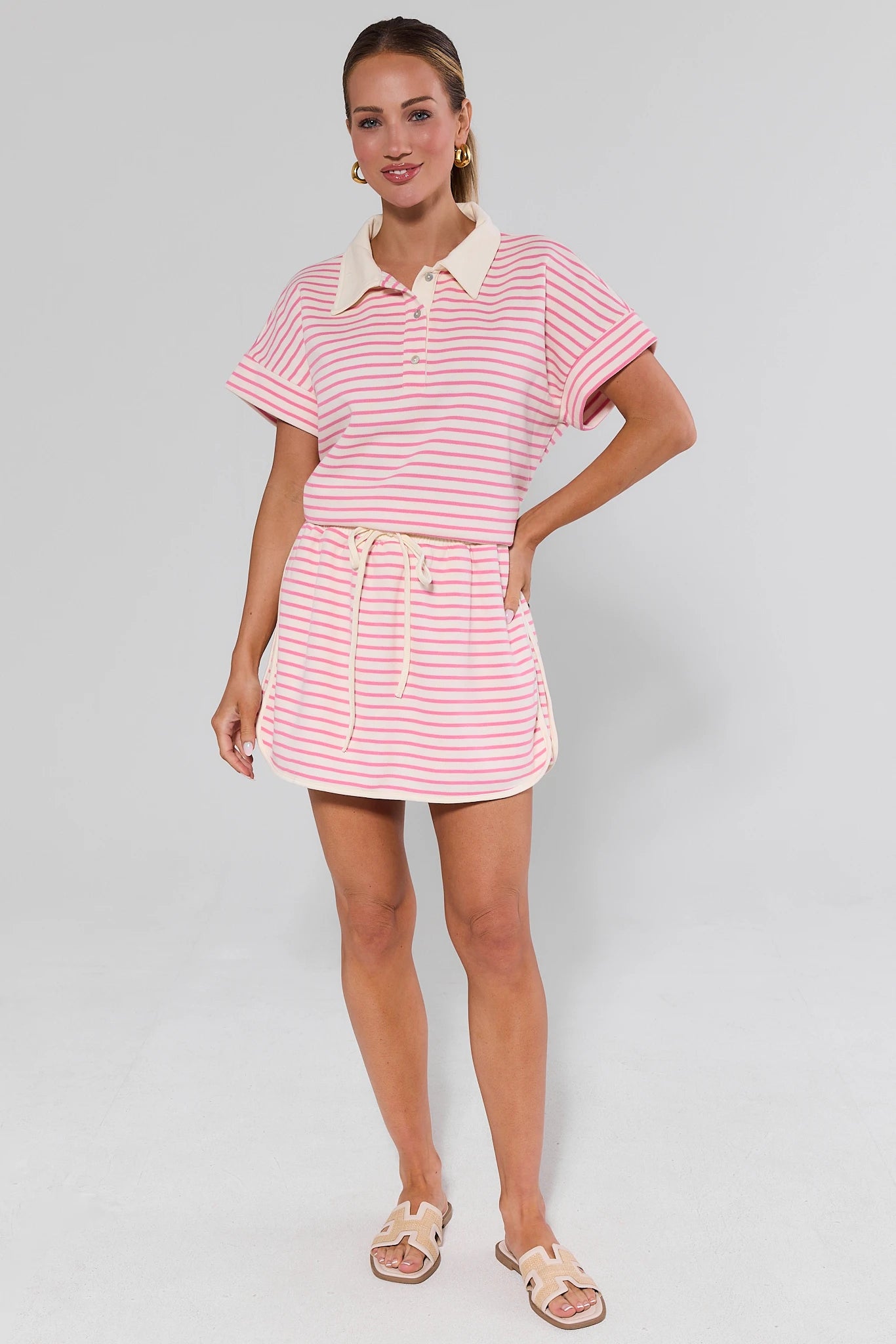 Woman wearing a pink and white striped dress with a collar on a gray background