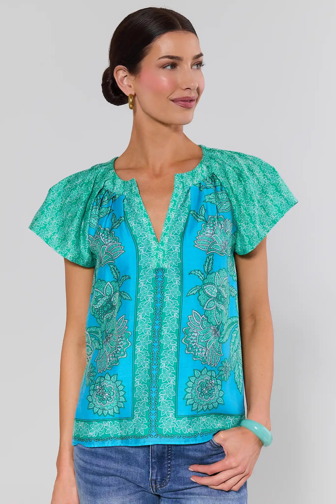 Woman wearing a teal and blue patterned sage top against a plain background