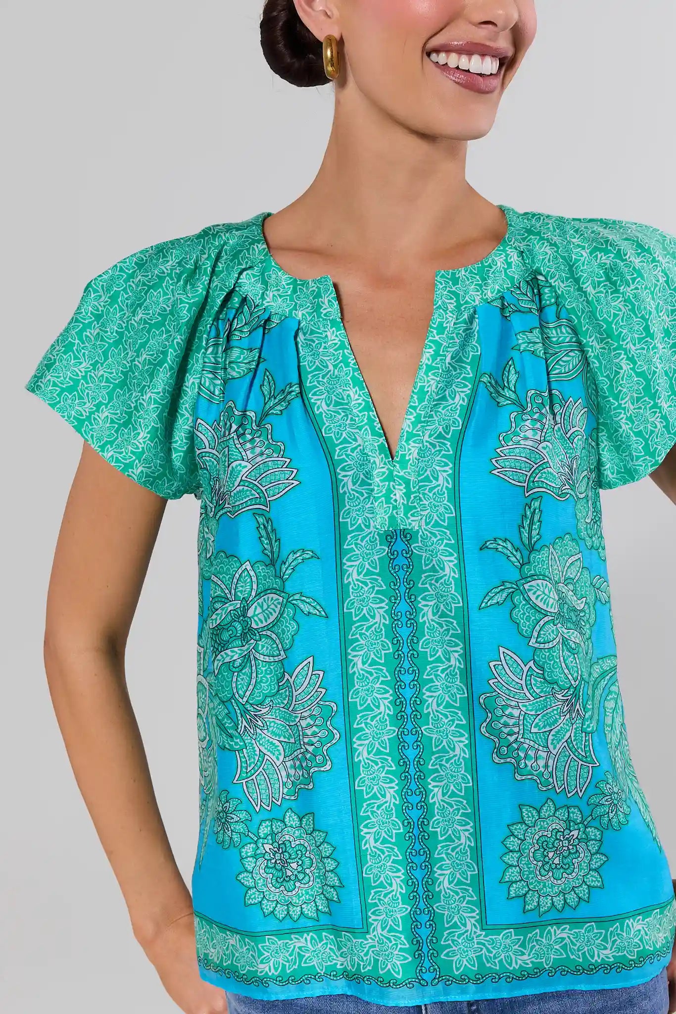 close up Woman wearing a turquoise blouse with green floral patterns on a plain background