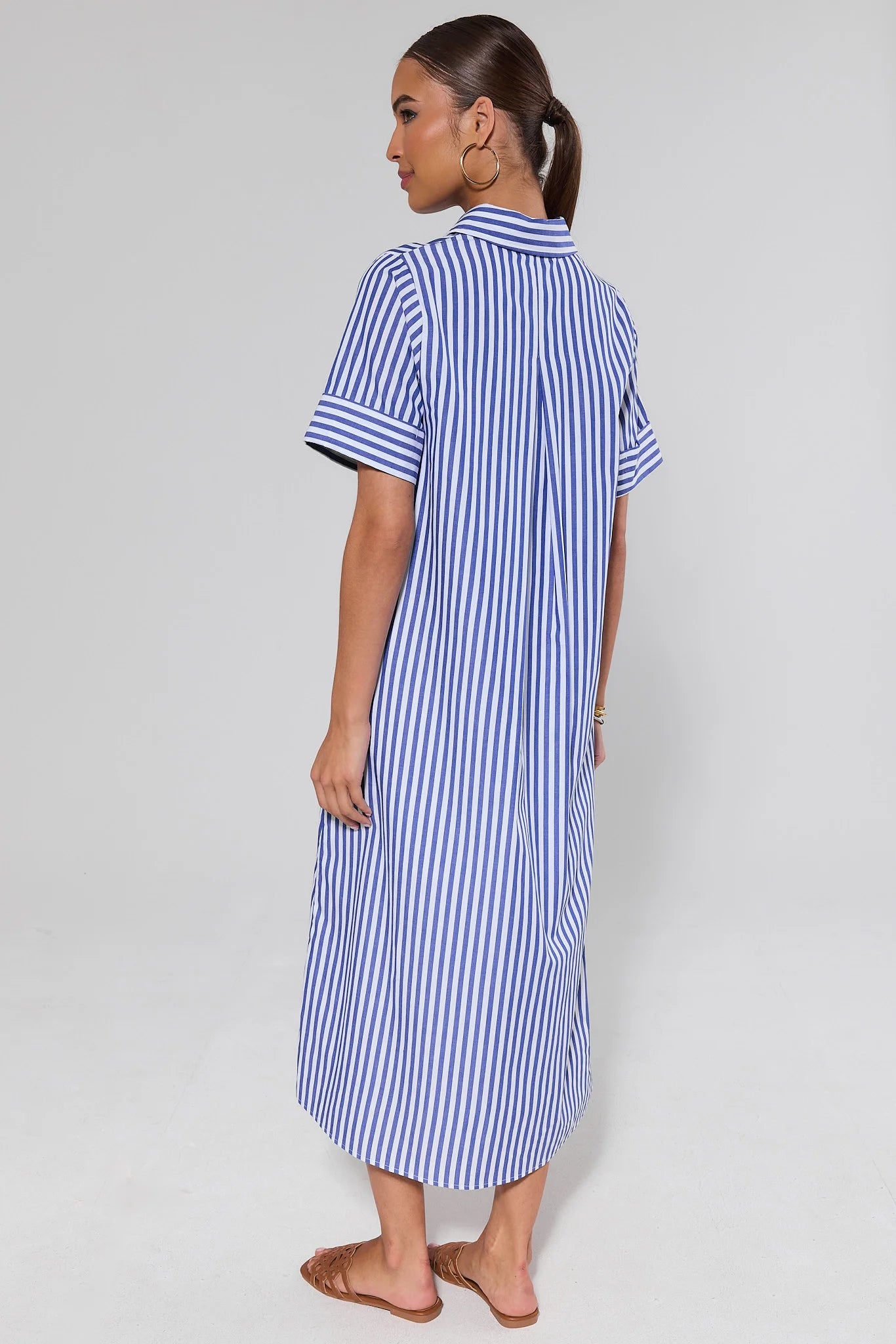 Woman standing wearing a blue and white striped dress against a plain background