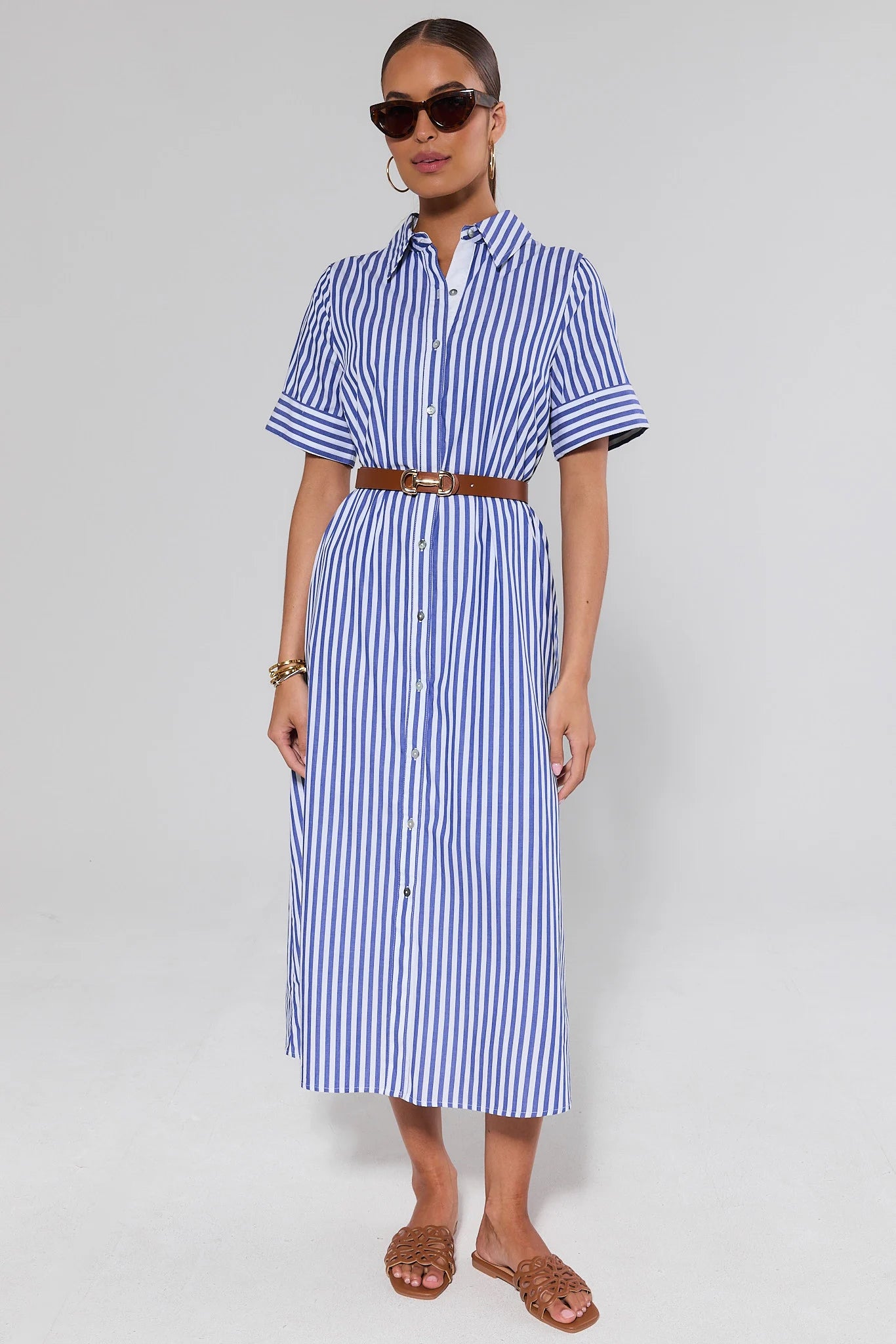 Woman wearing a blue and white striped juniper dress with a brown belt on a plain background