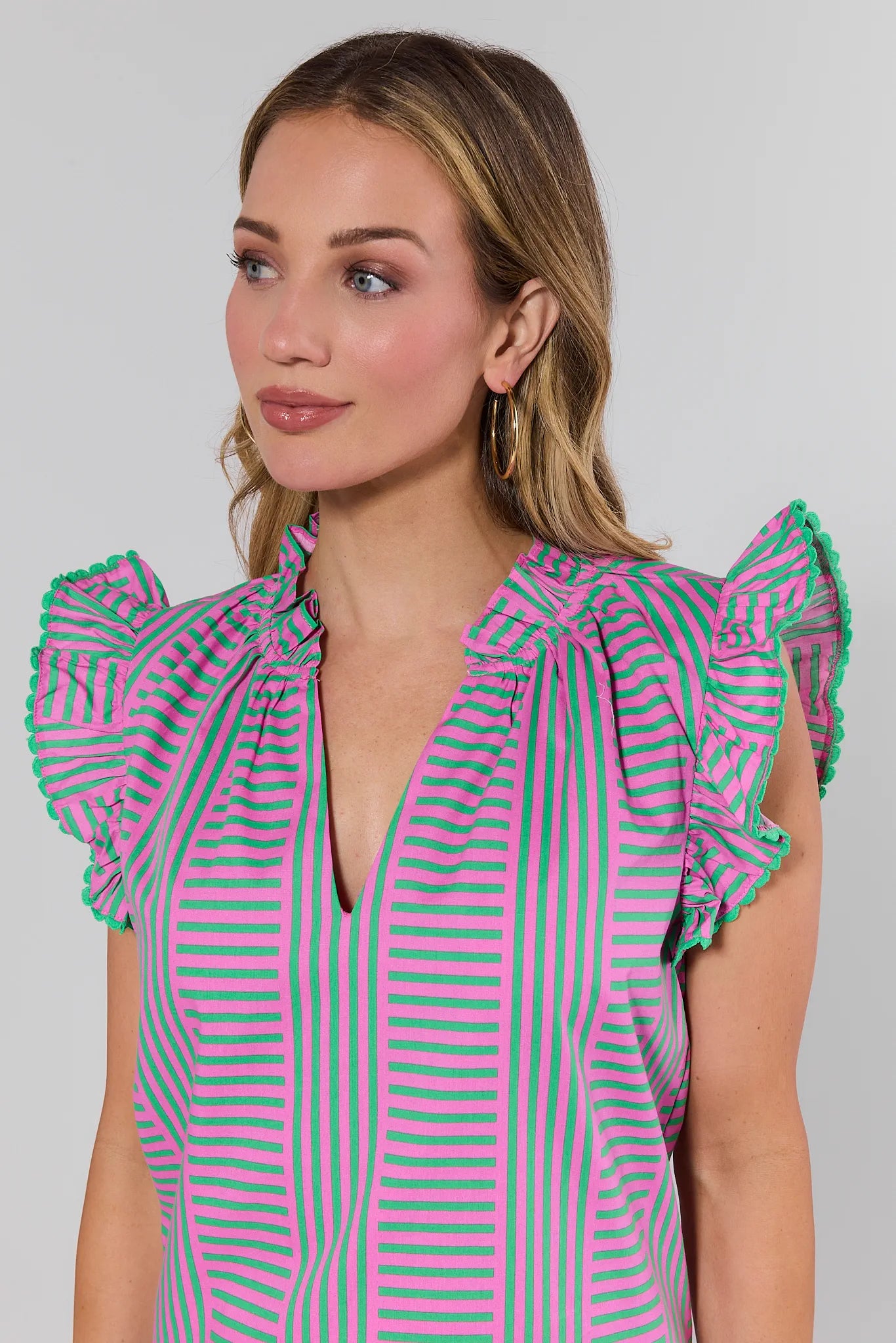 Woman wearing a pink and green striped blouse with ruffled sleeves on a gray background