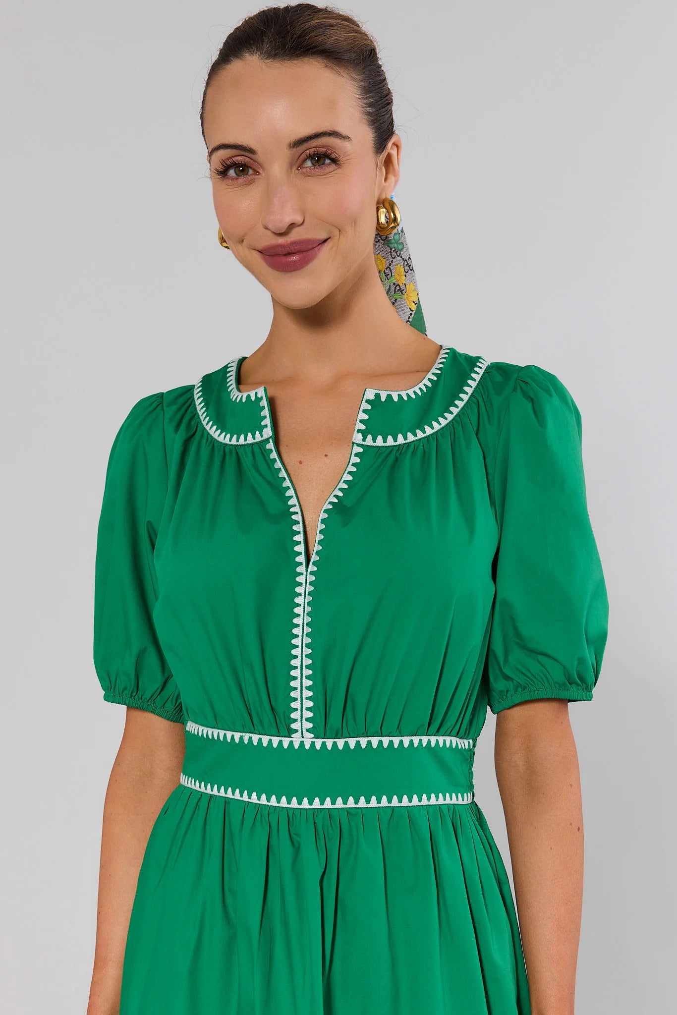 close up Woman wearing a green dress with white trim against a plain background