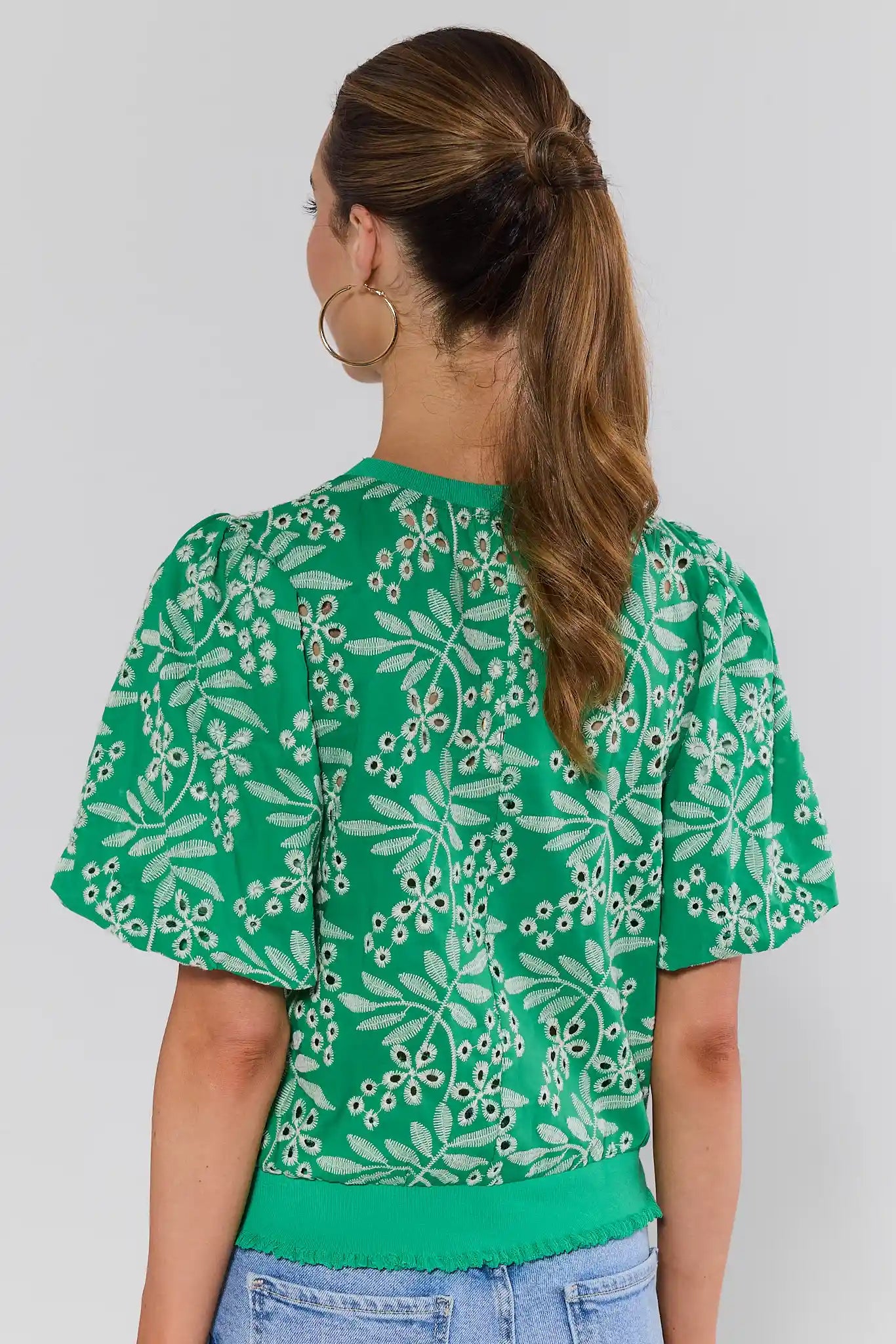 Woman standing wearing a green floral blouse against a plain background