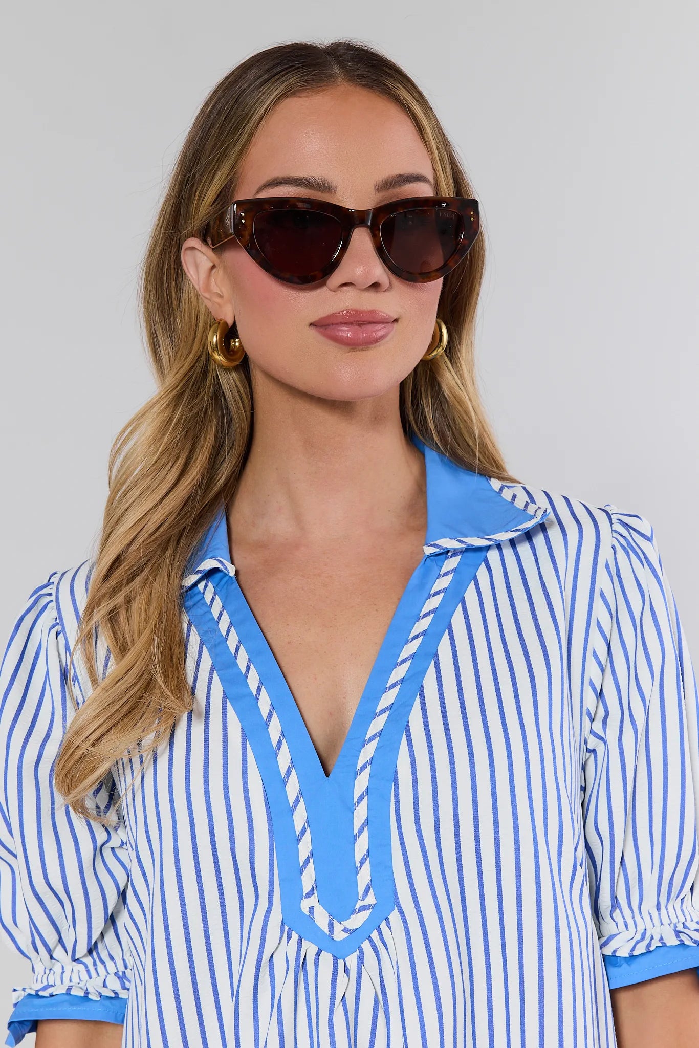 Woman wearing a blue and white striped dress with sunglasses against a gray background