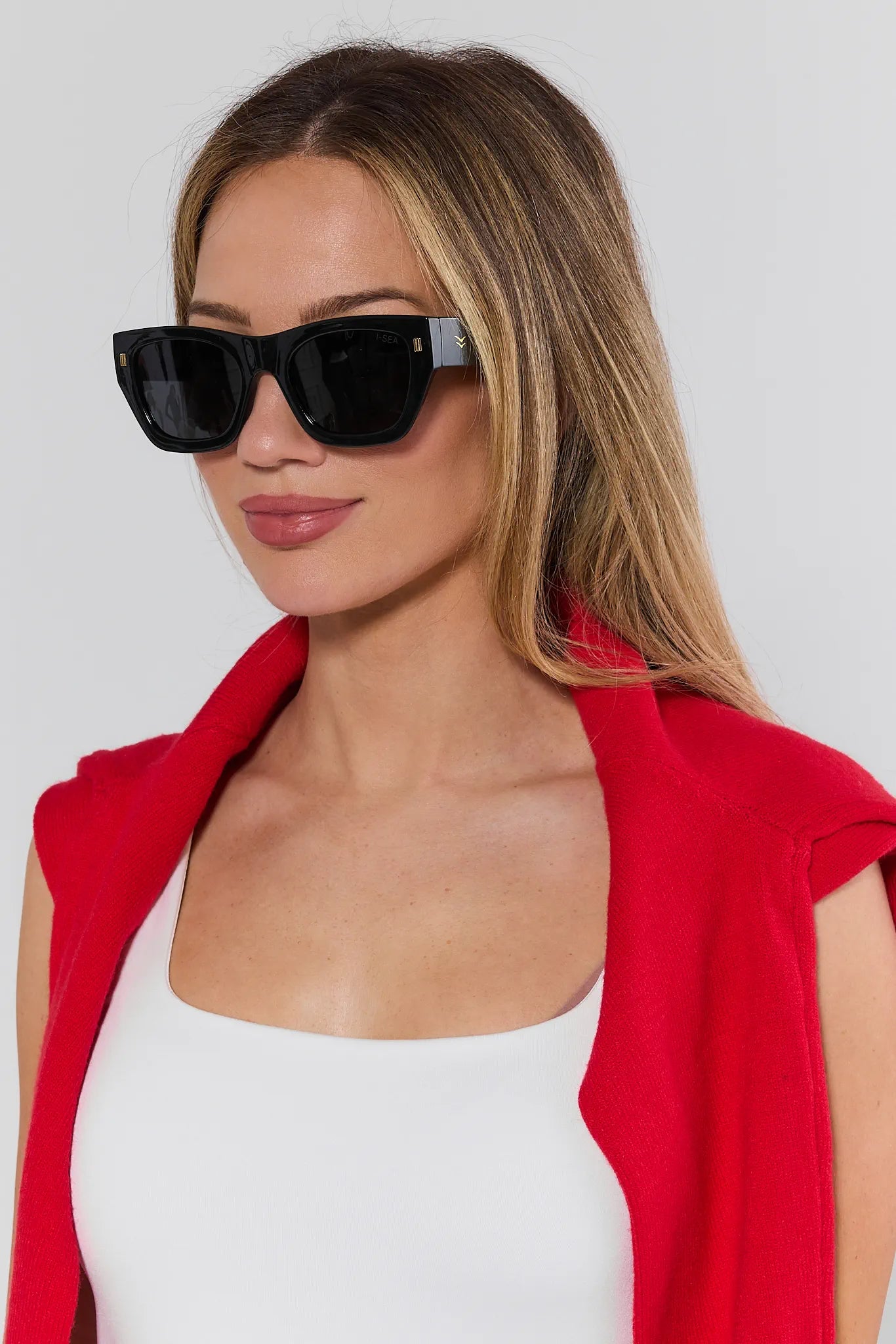 Woman wearing black sunglasses and a red jacket against a white background