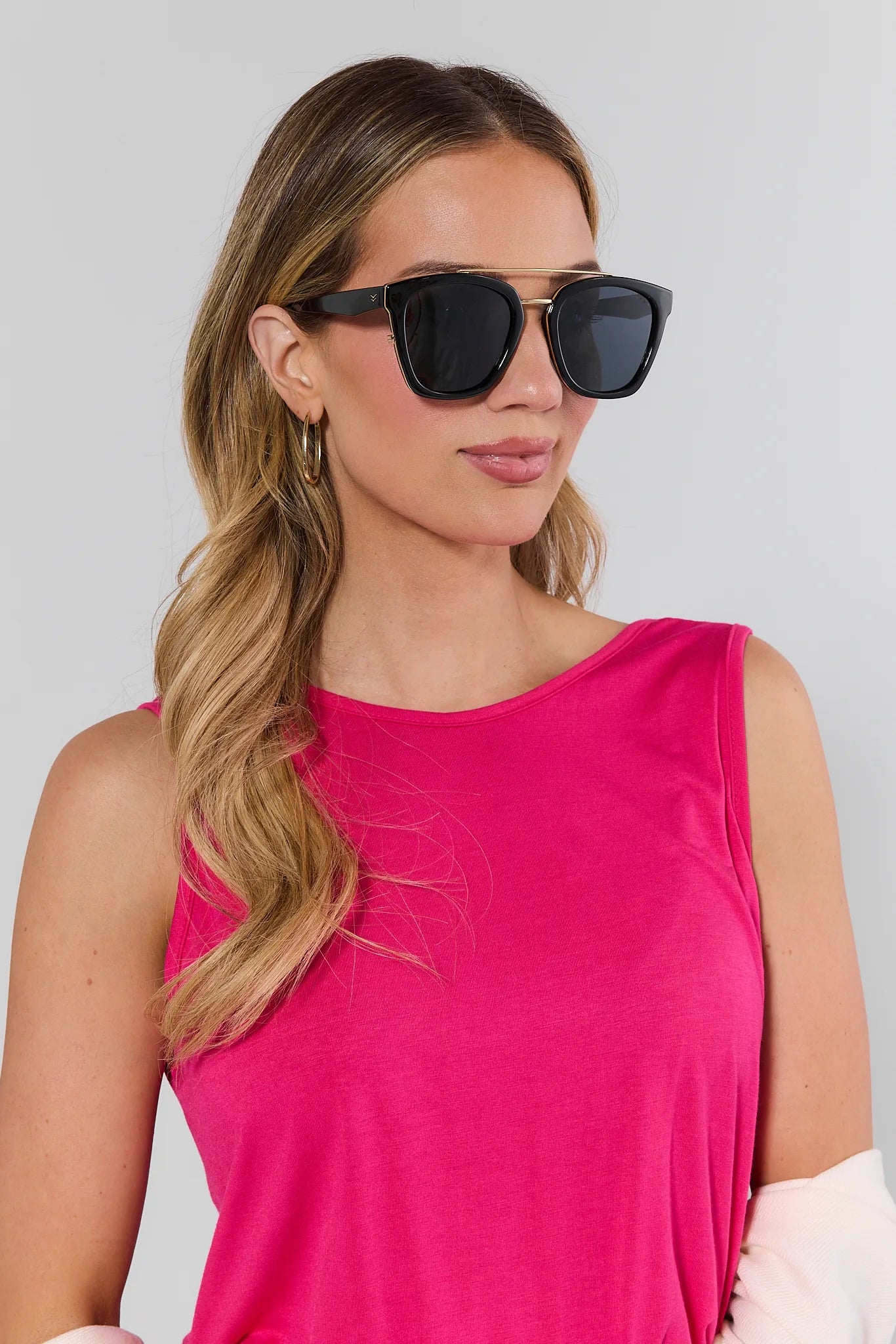 Woman wearing a bright pink sleeveless top and black sunglasses against a plain background