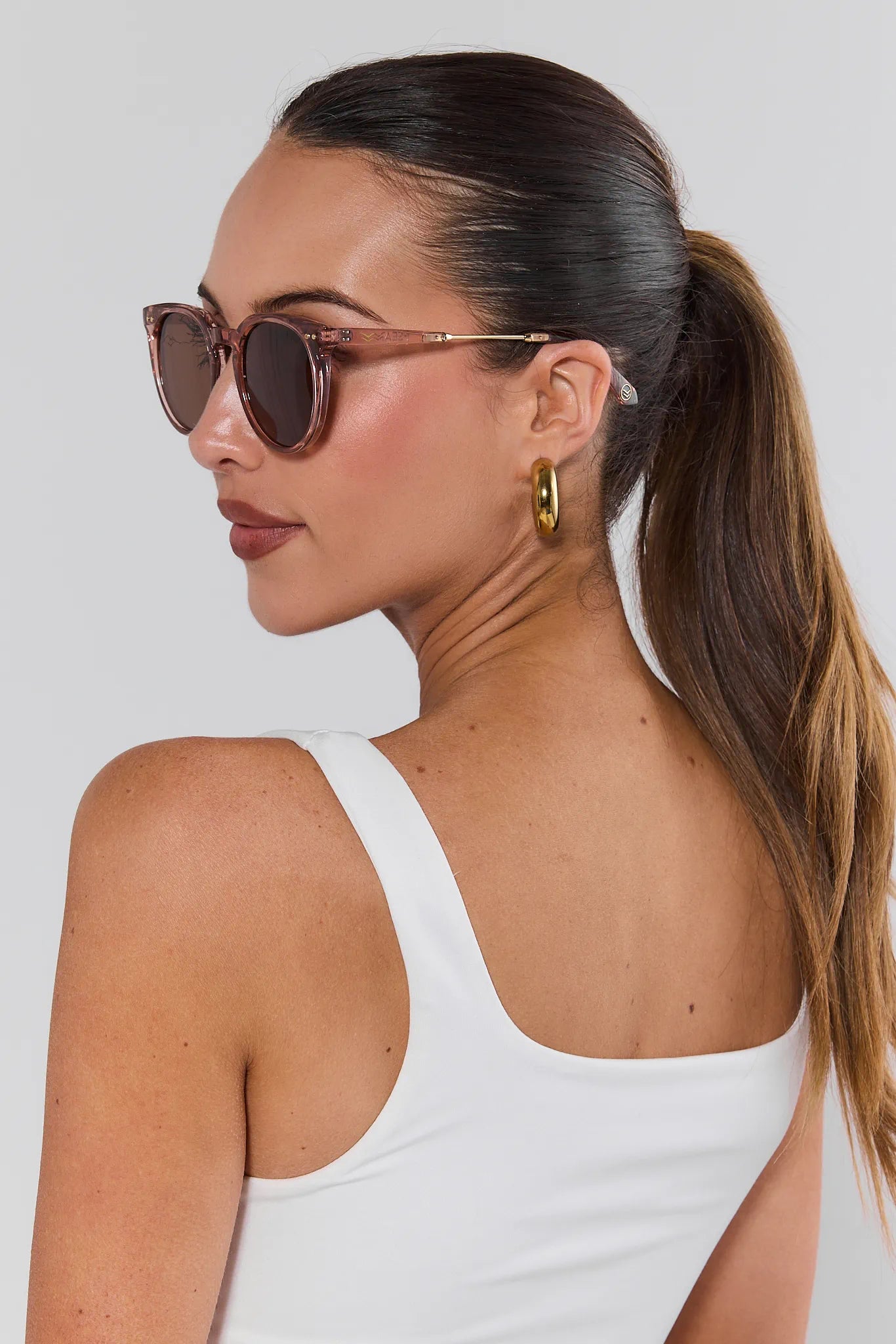 Woman wearing sunglasses and a white tank top with a plain background