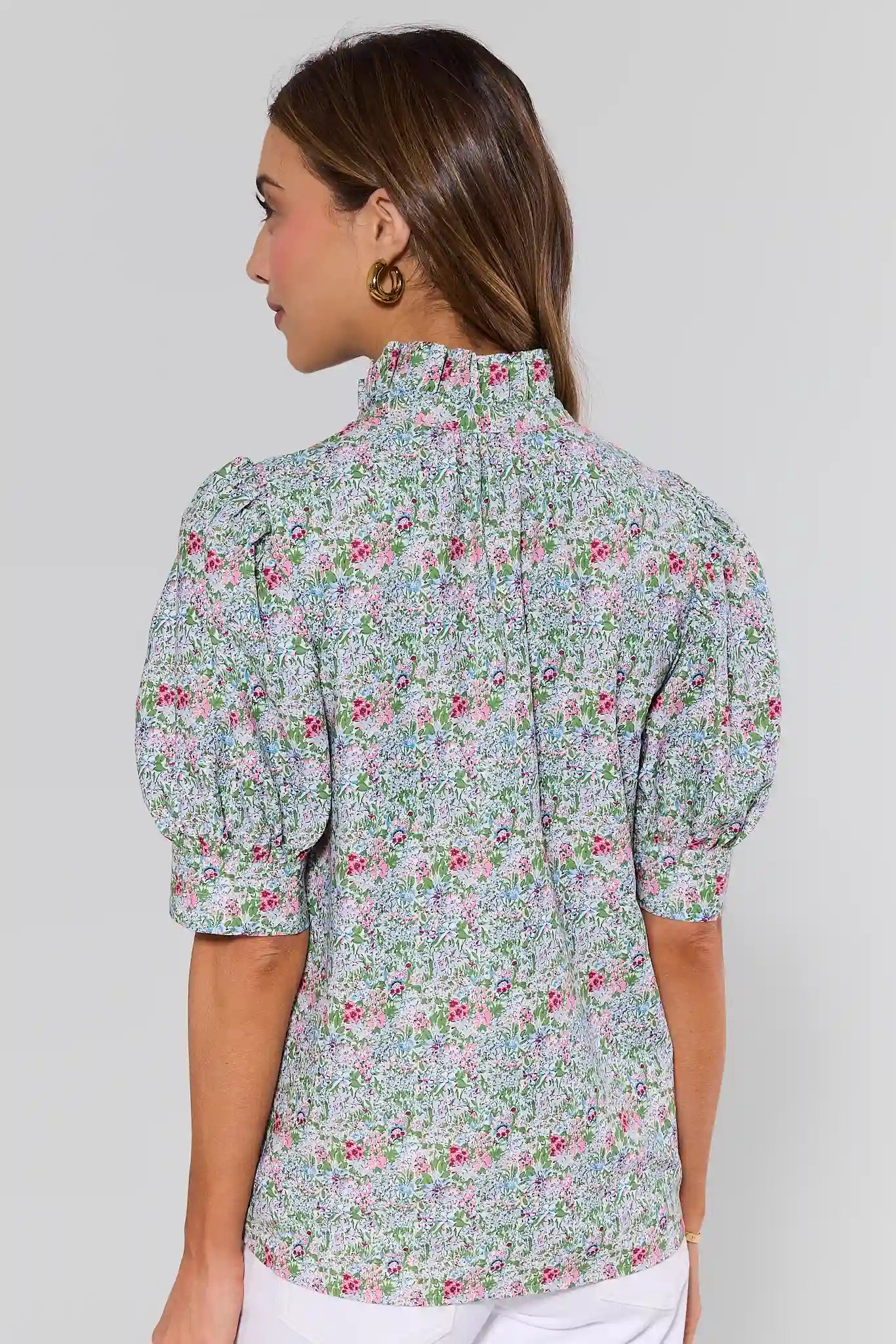 Woman standing wearing a floral blouse against a plain background