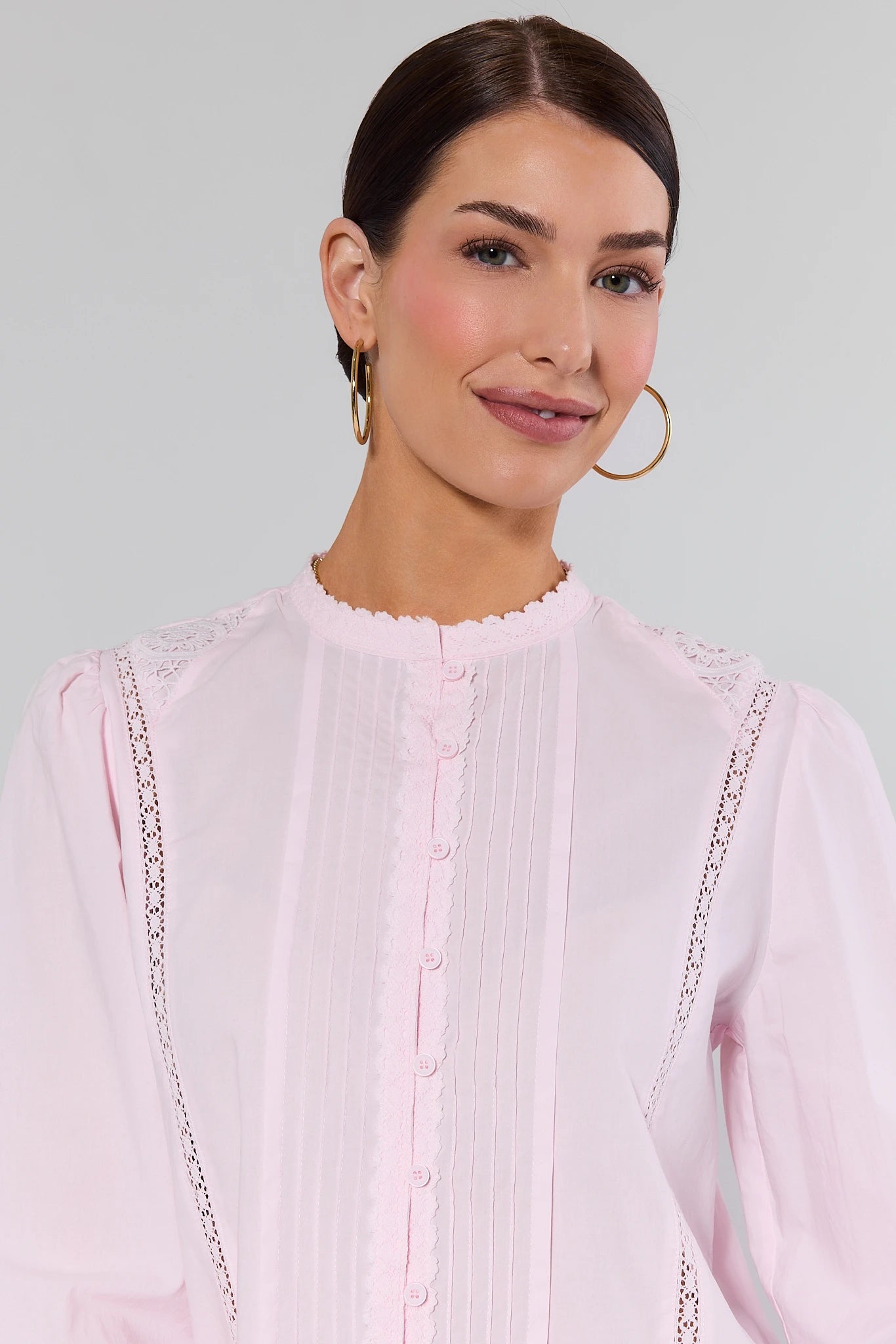 close up Woman wearing a light pink blouse with lace details on a plain background