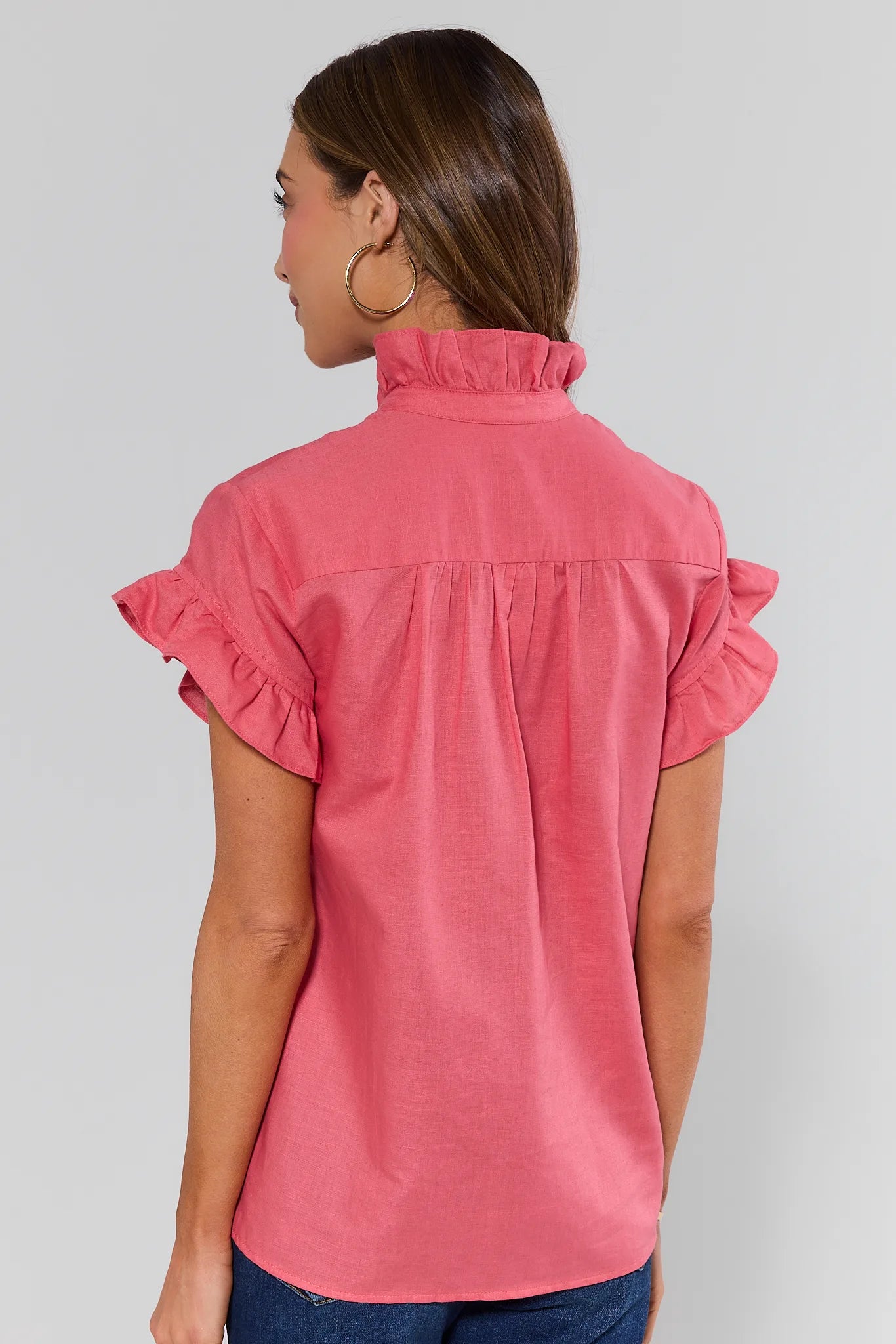 Woman standing wearing a pink blouse with ruffled sleeves on a plain background