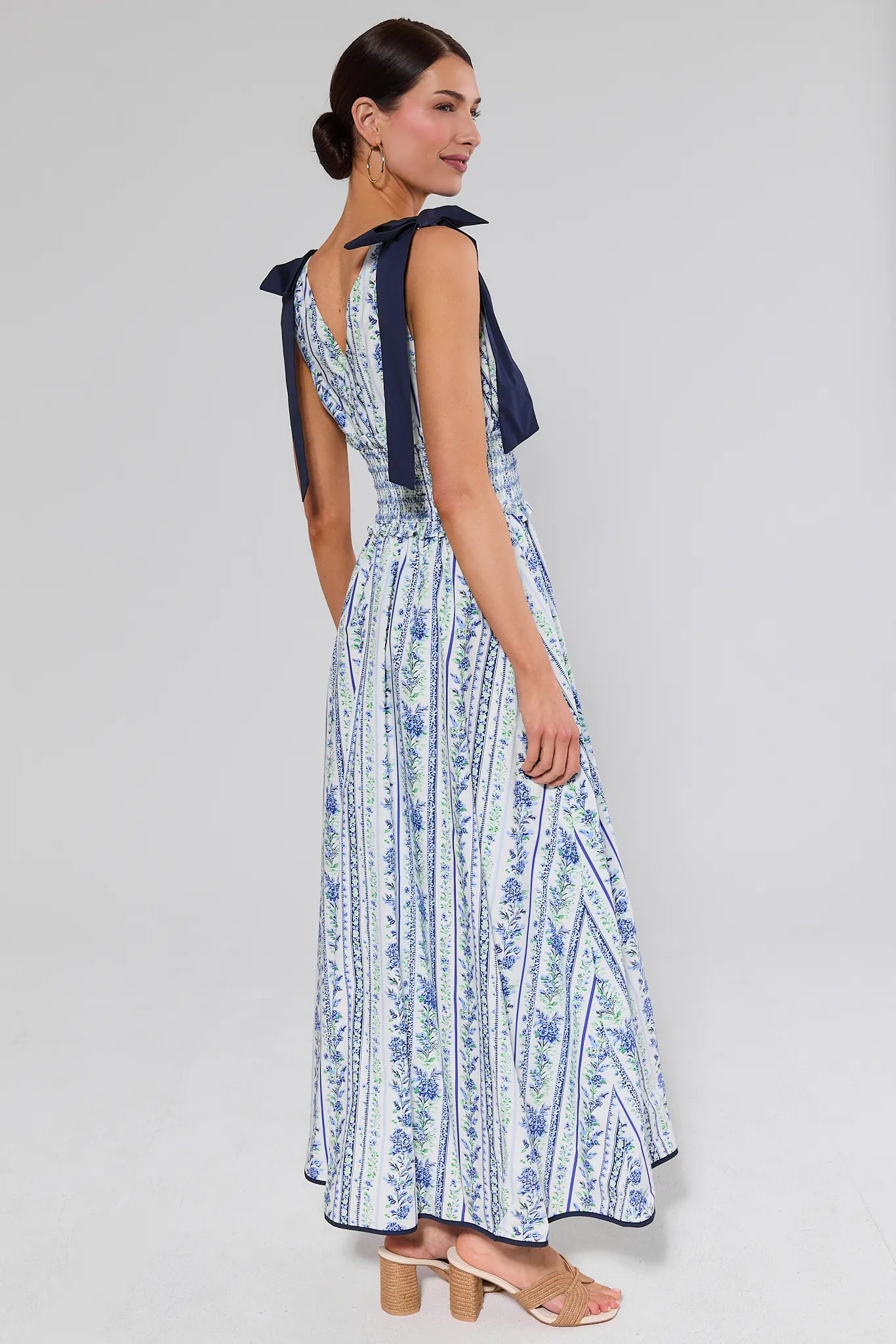 Woman standing wearing a blue and white patterned dress with a bow detail on a gray background