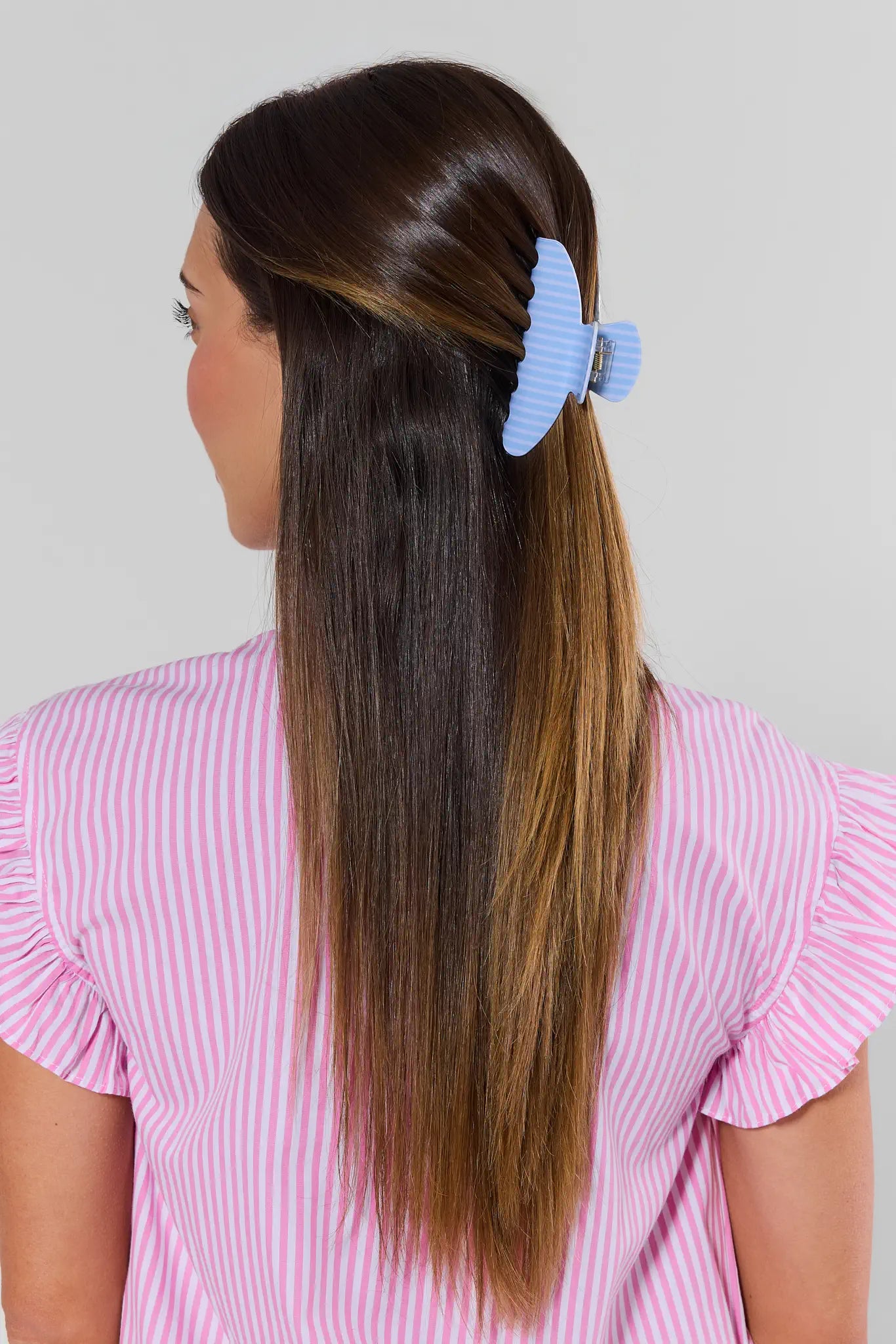 Person with long hair tied back with a blue scrunchie against a plain background