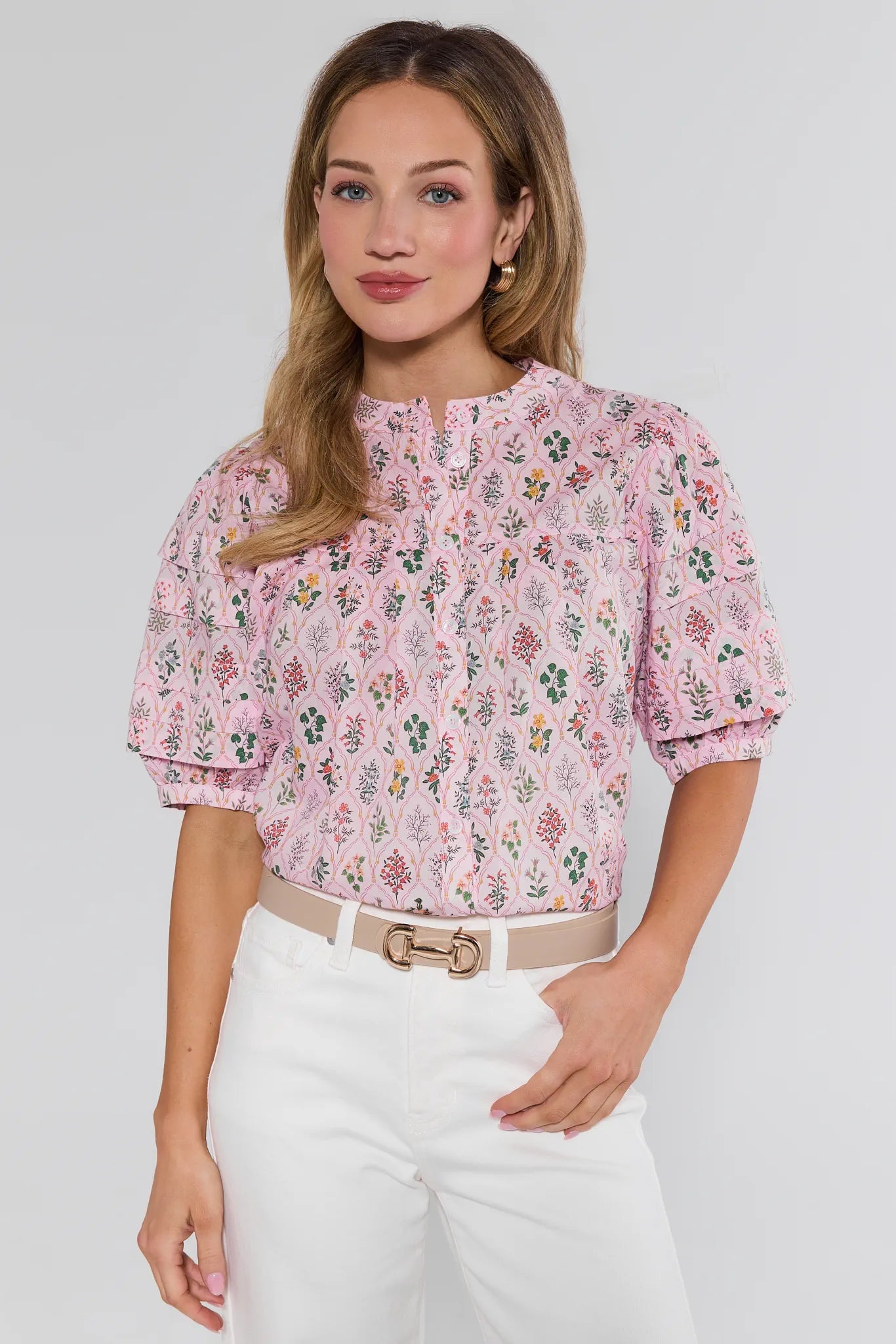 Woman wearing a pink floral blouse and white pants on a light gray background