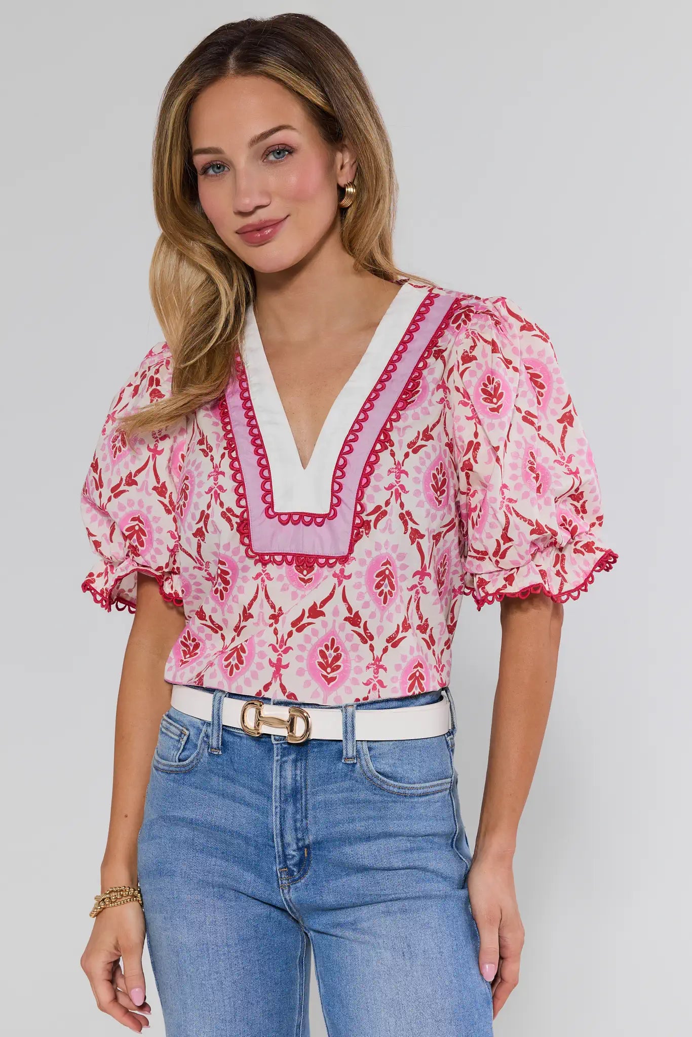 Woman wearing a pink floral blouse with white trim and blue jeans on a plain background