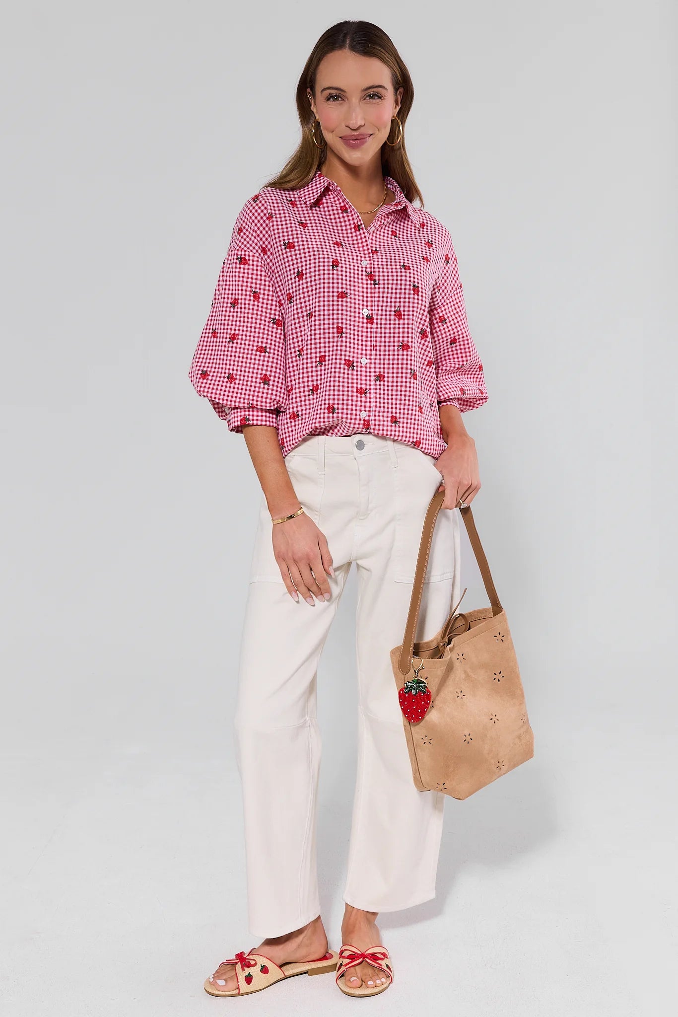 Woman wearing a red checkered shirt and white pants, holding a beige handbag on a light gray background