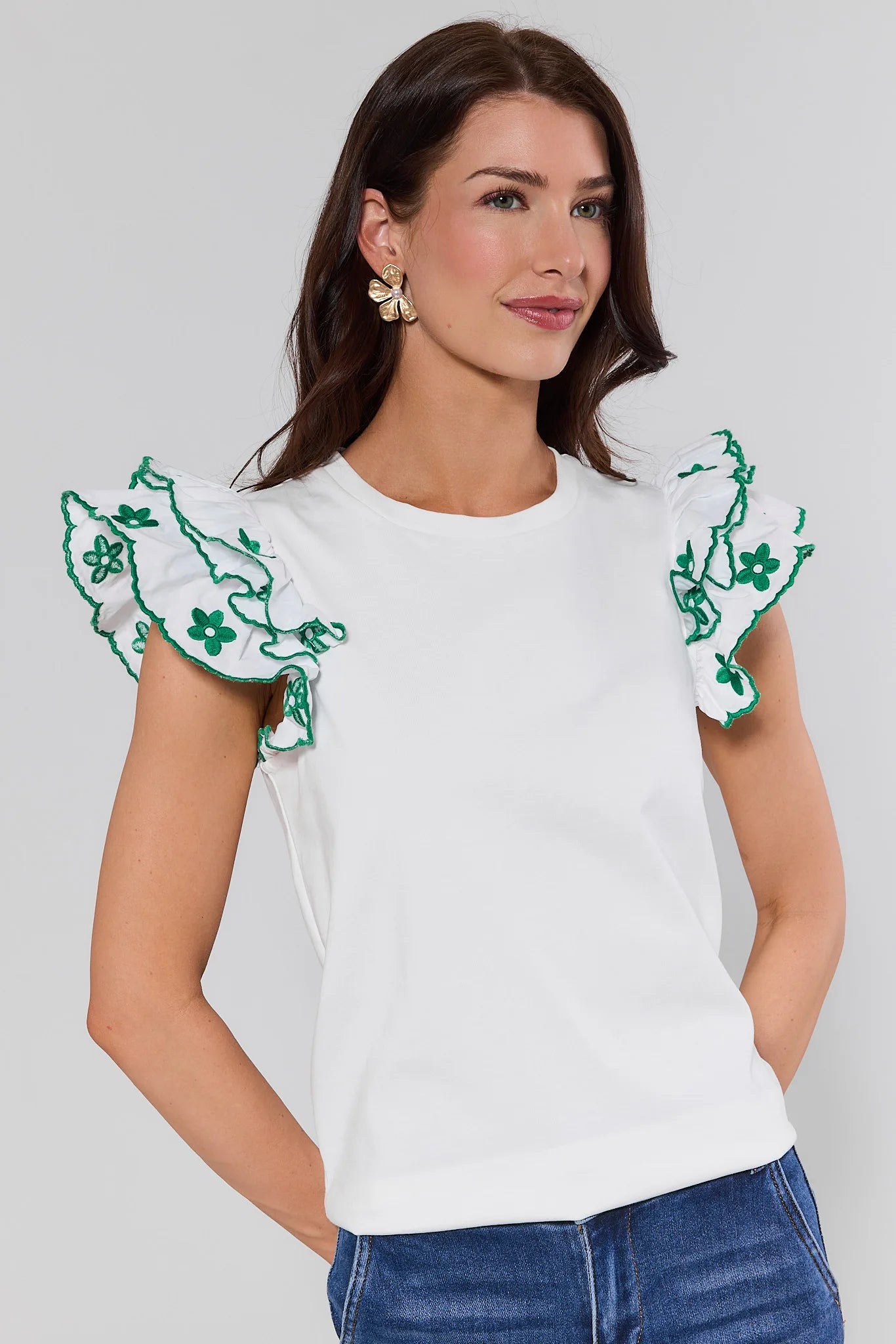 Woman wearing a white top with green floral embroidery on sleeves against a plain background