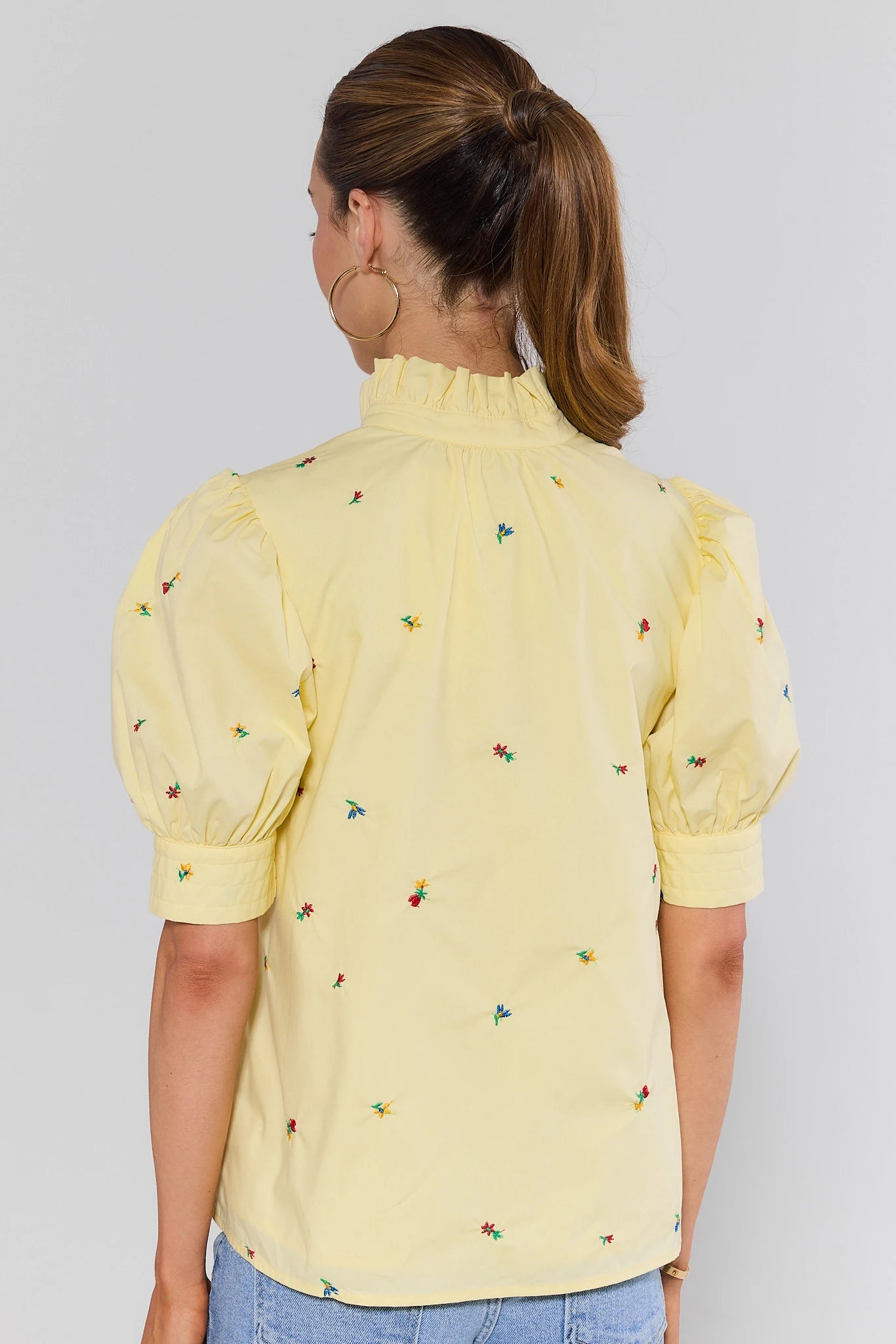 Woman wearing a yellow blouse with floral embroidery on a plain background