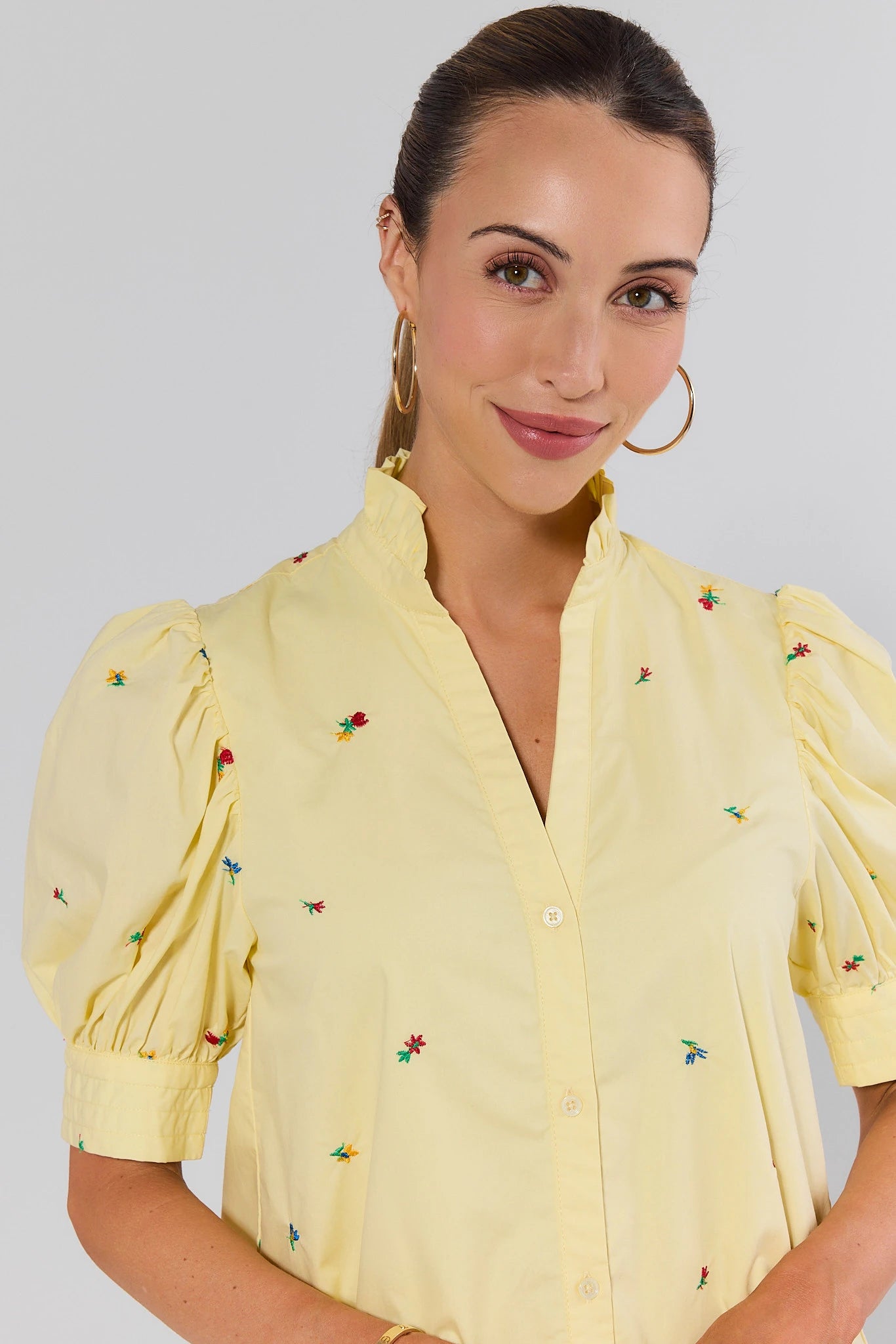 close up Woman wearing a yellow blouse with floral embroidery on a plain background