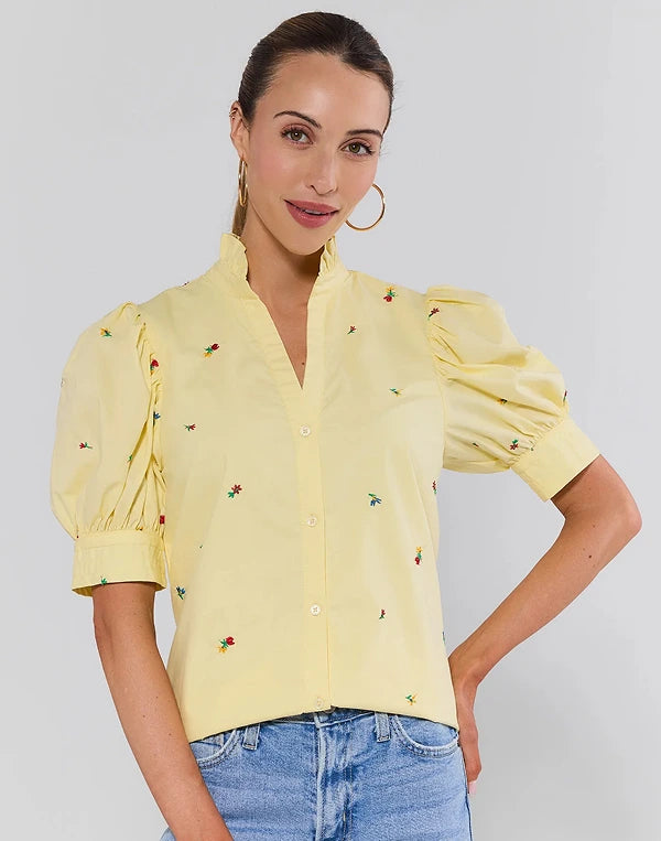 Woman wearing a yellow blouse with floral embroidery on a plain background