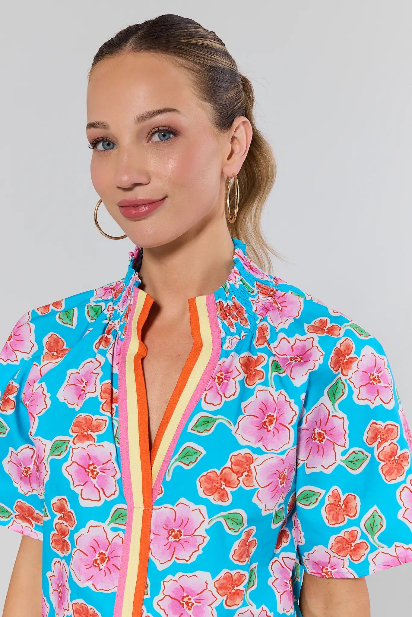 Woman wearing a colorful floral zip-up shirt against a plain background close up