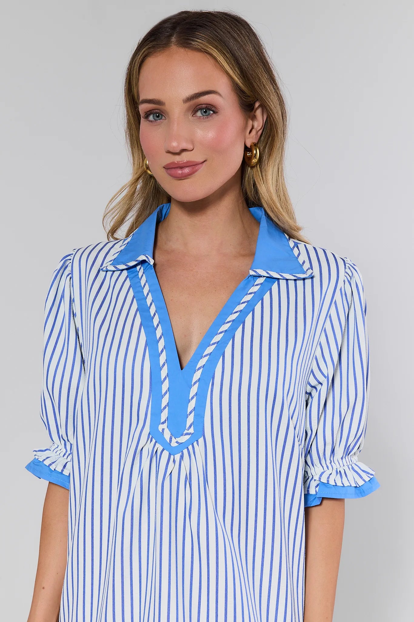Woman wearing a blue and white striped dress with a deep neckline on a gray background