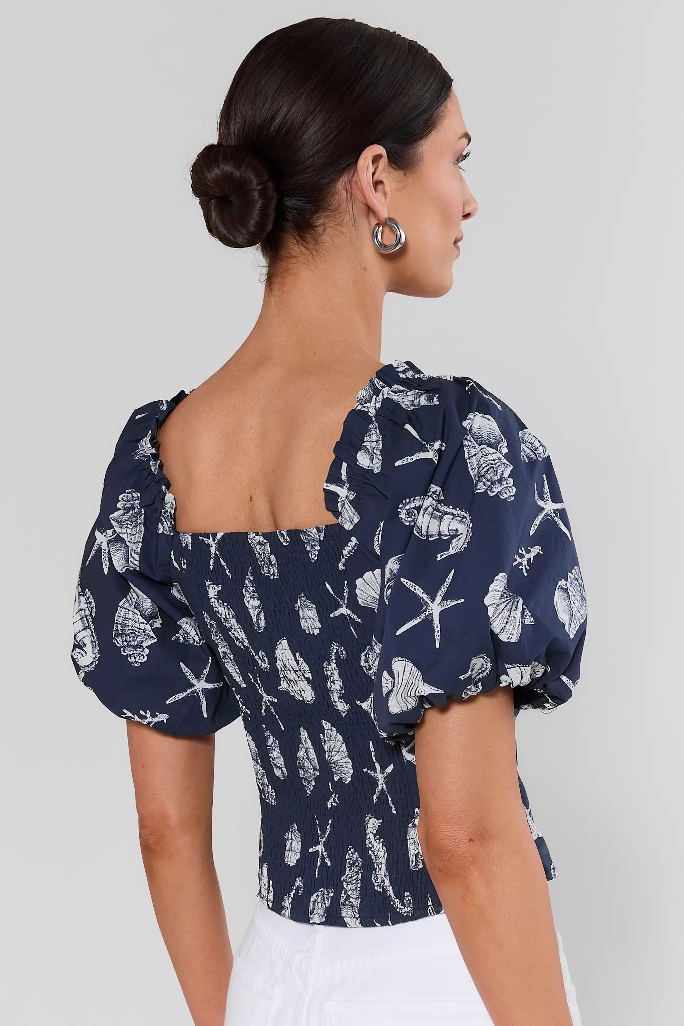Woman standing wearing a navy blue blouse with white shell pattern on a plain background