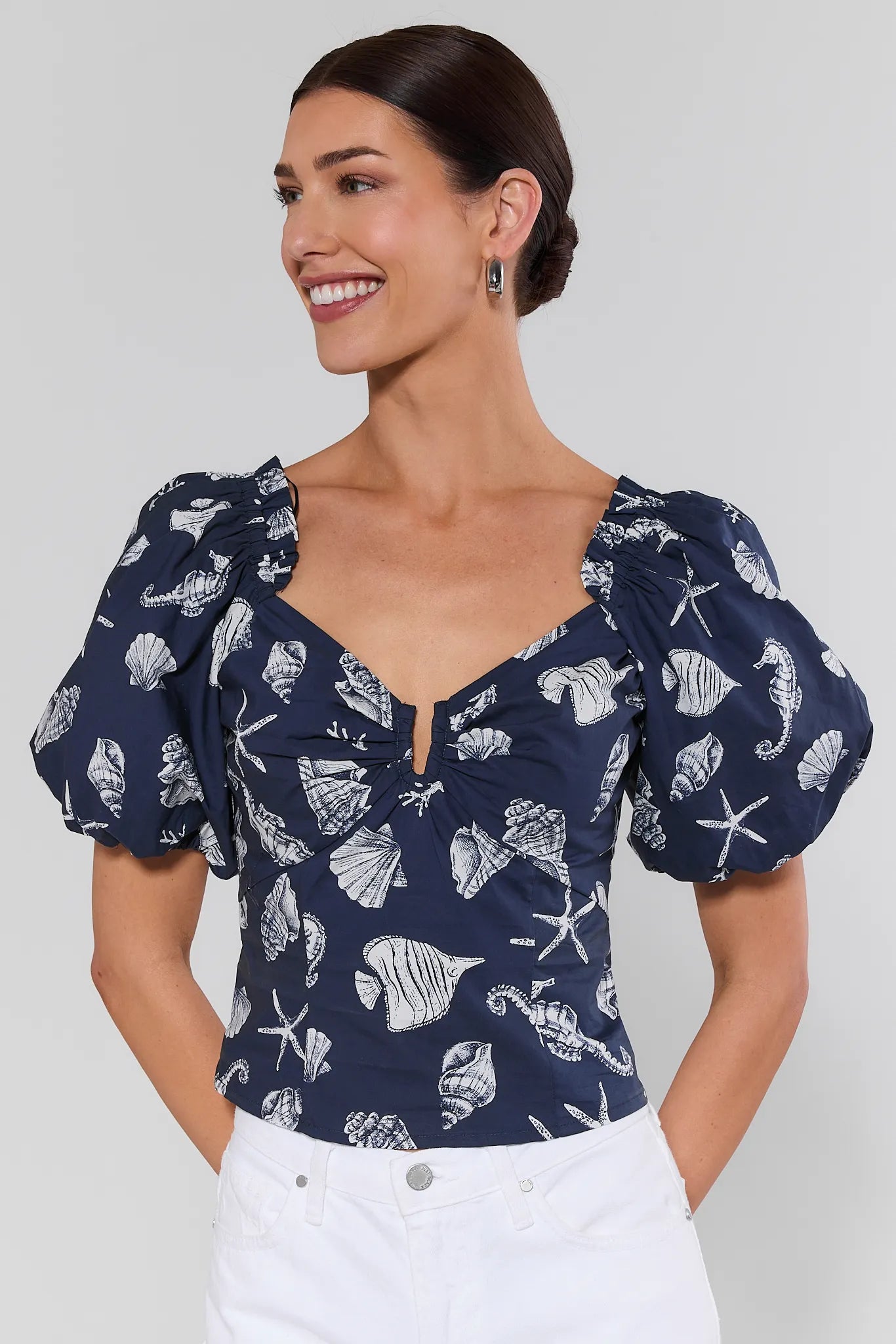 Woman wearing a navy blue top with white sea-themed print on a plain background