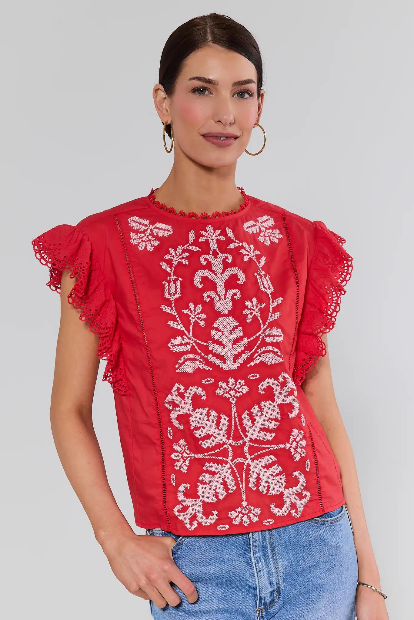 Woman wearing a red blouse with white embroidery on a plain background
