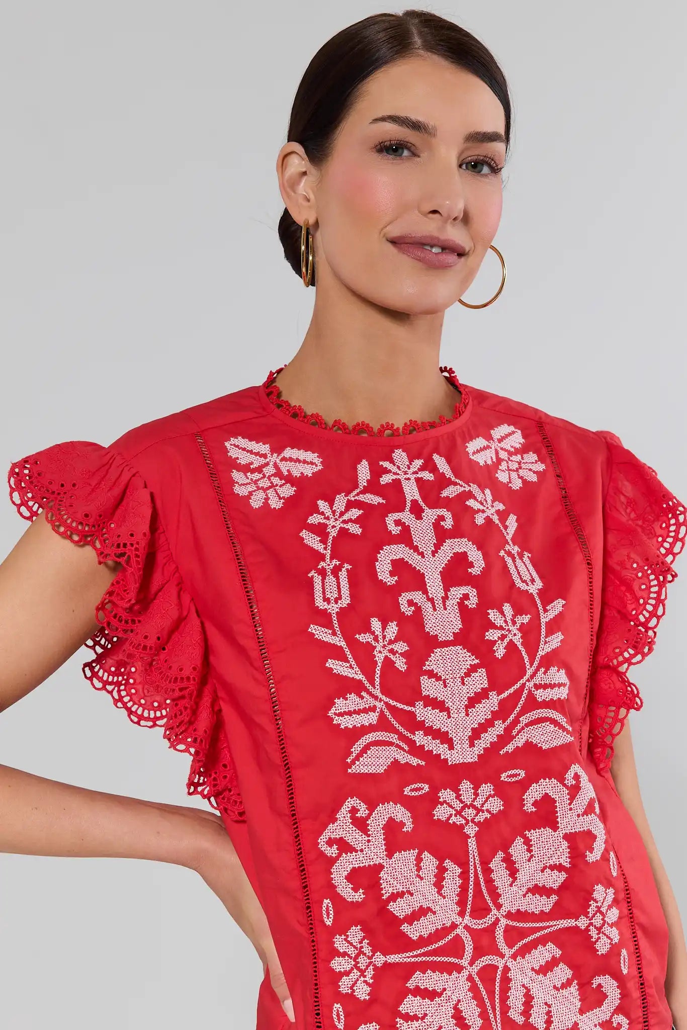close up Woman wearing a red dress with white floral embroidery on a plain background