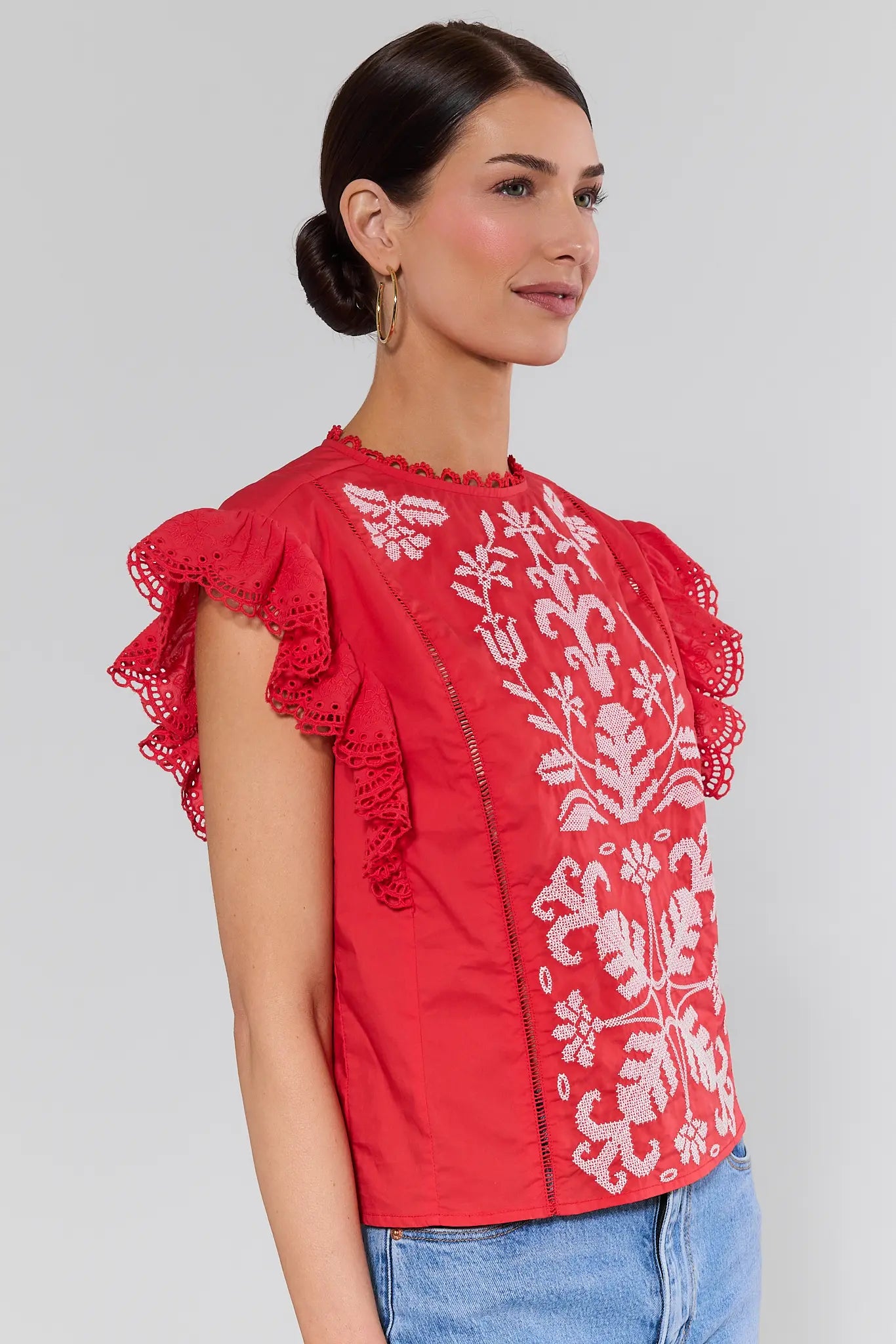 side shot Woman wearing a red blouse with white floral embroidery on a plain background