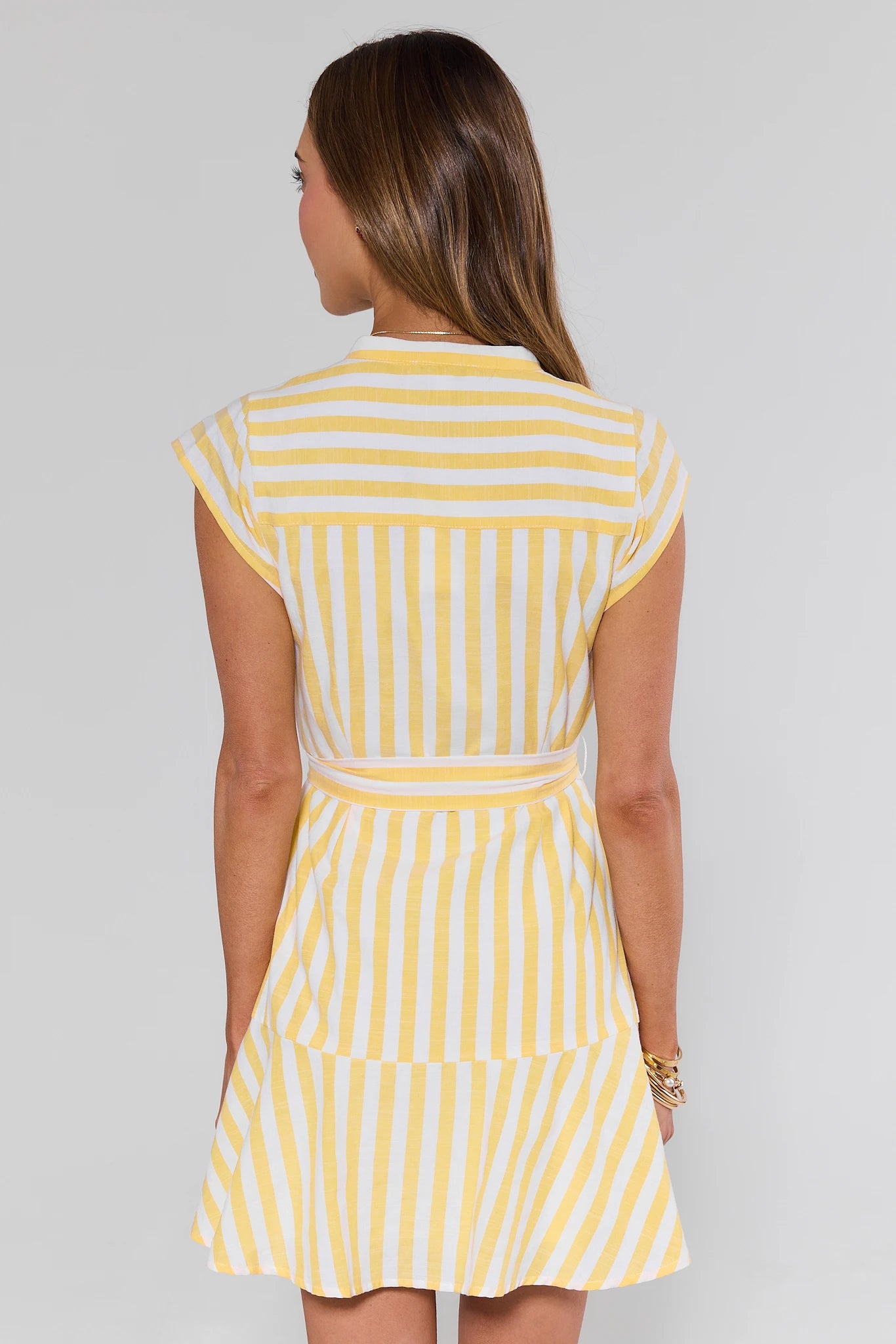 Woman standing wearing a yellow and white striped dress on a gray background