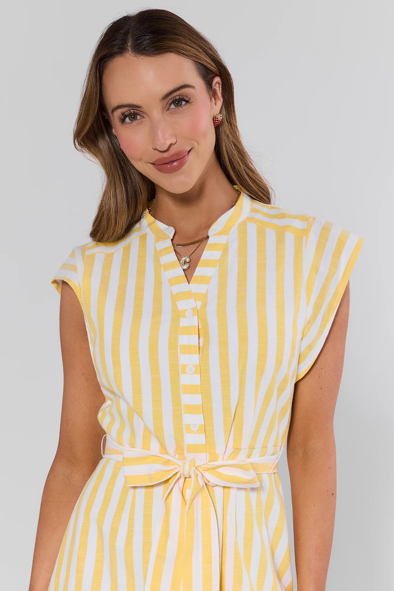 close up Woman wearing a yellow and white striped dress against a plain background