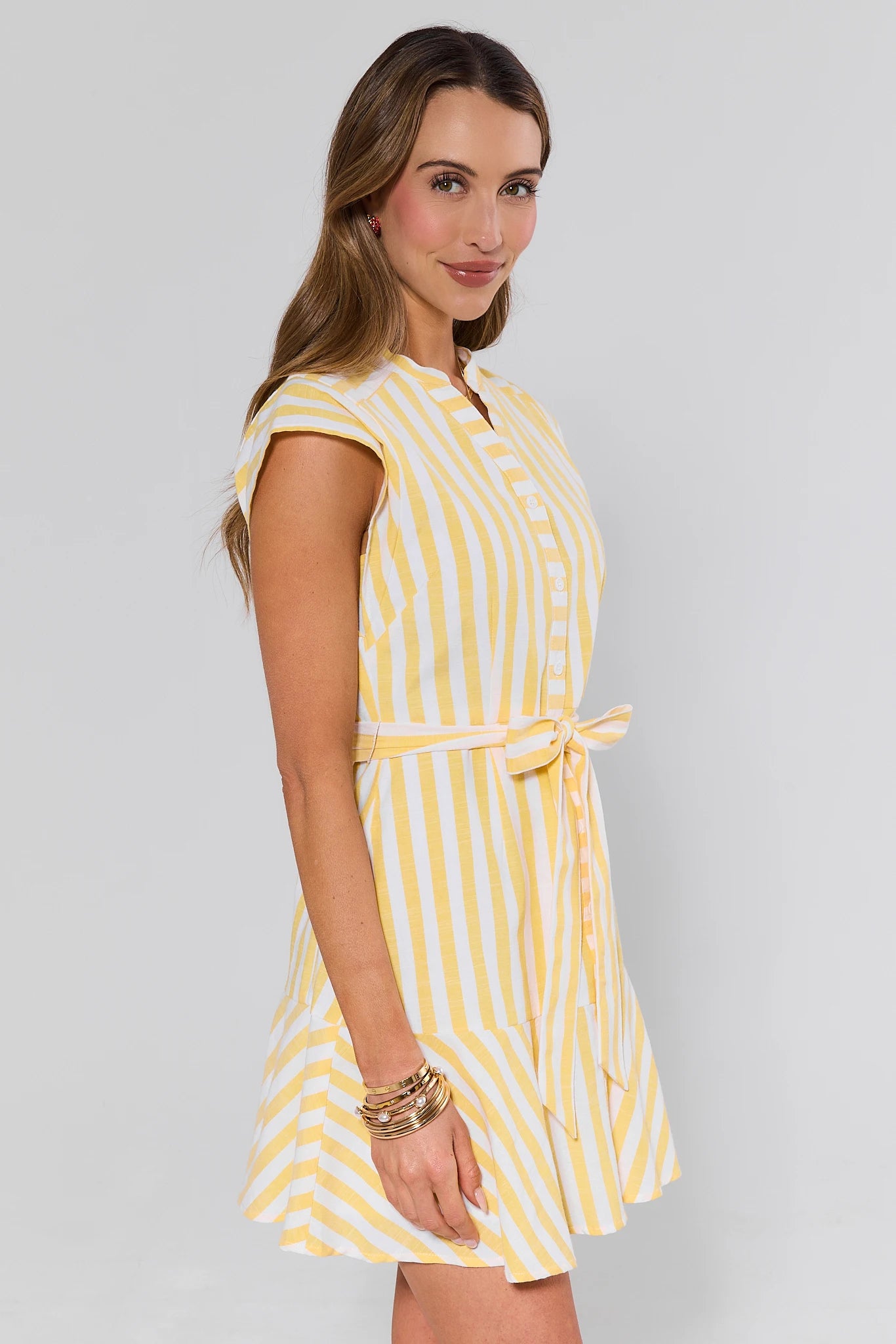 side shot Woman wearing a yellow and white striped dress on a gray background