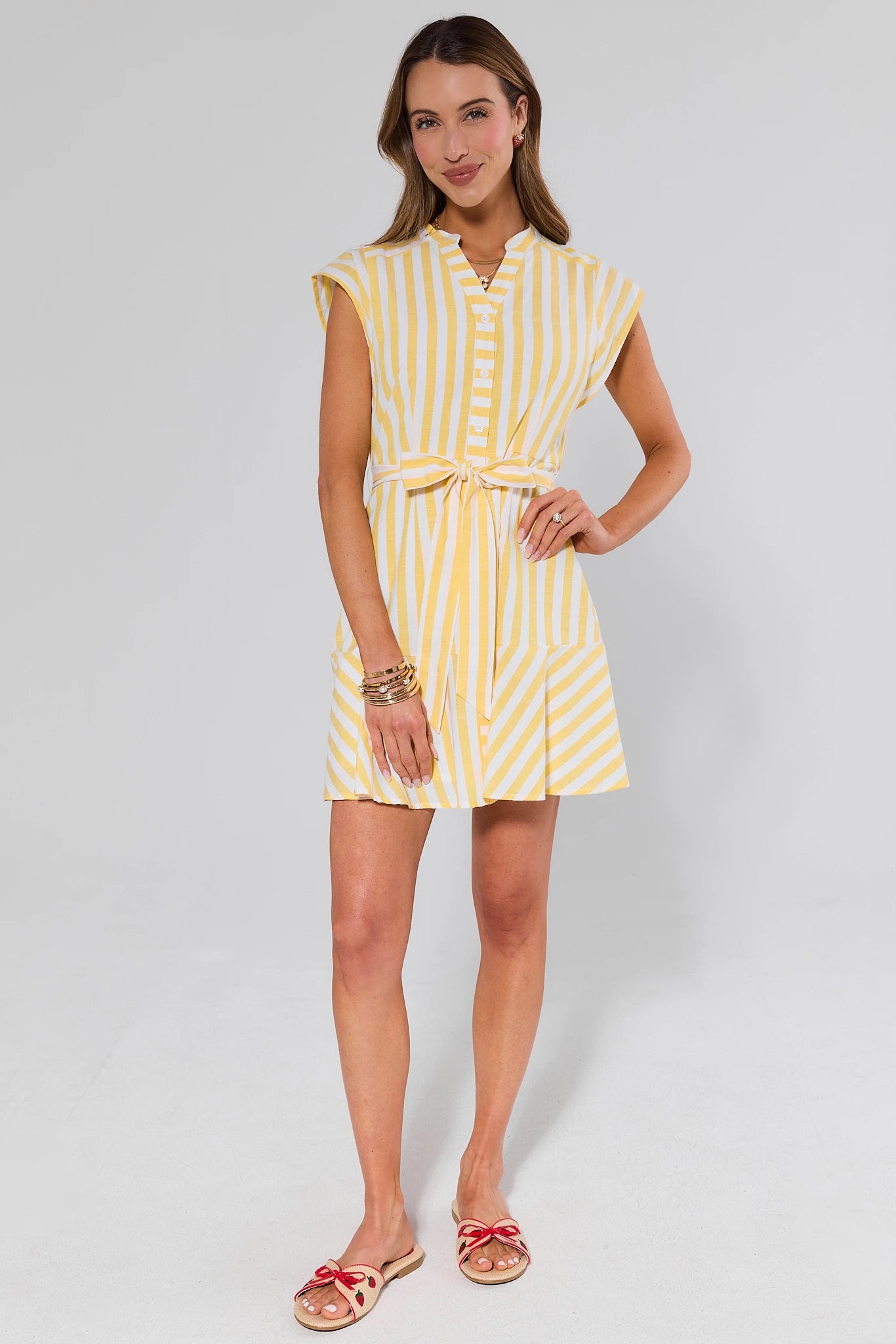 Woman wearing a yellow and white striped dress and flats on a plain background