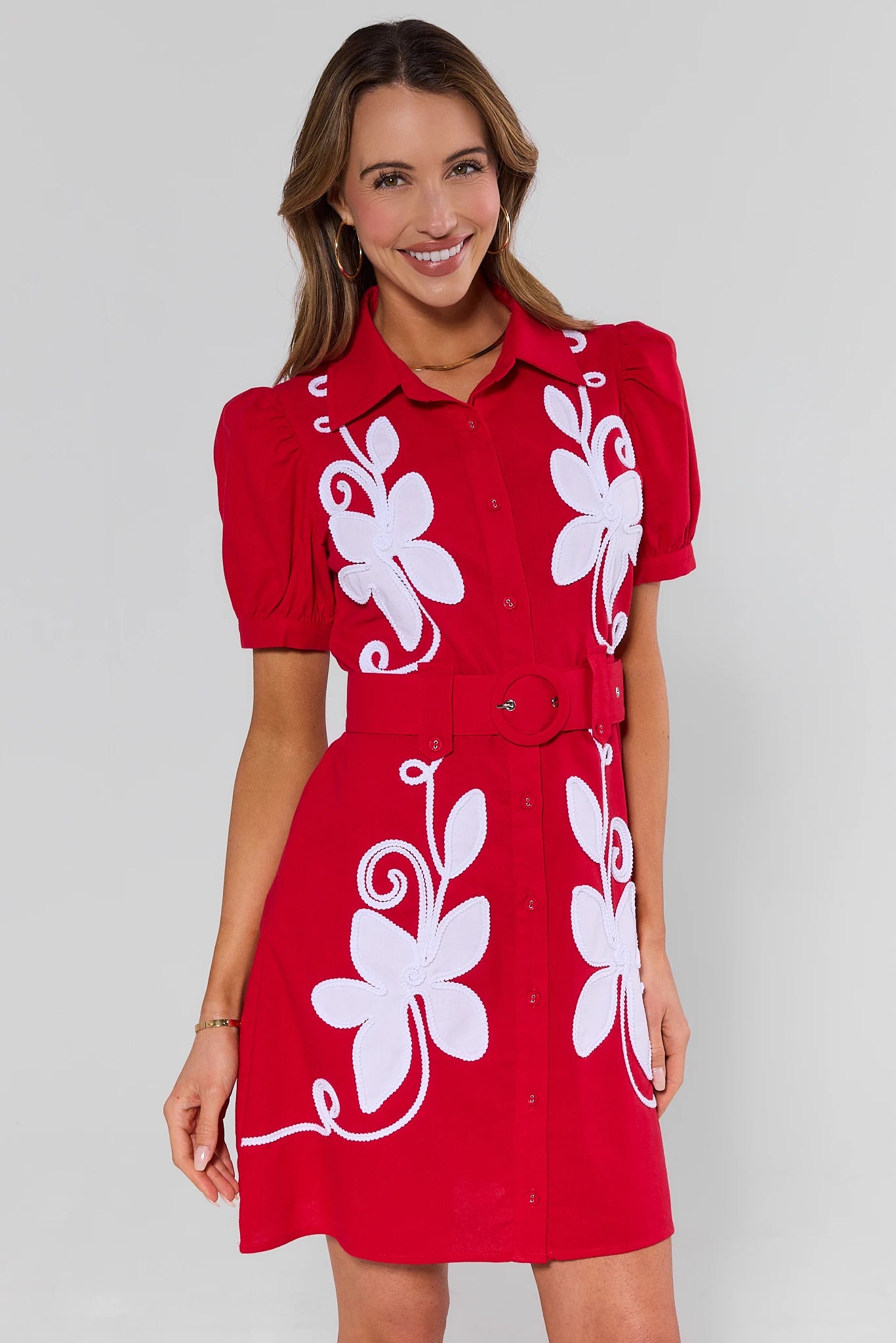 Woman wearing a red dress with white floral patterns on a plain background