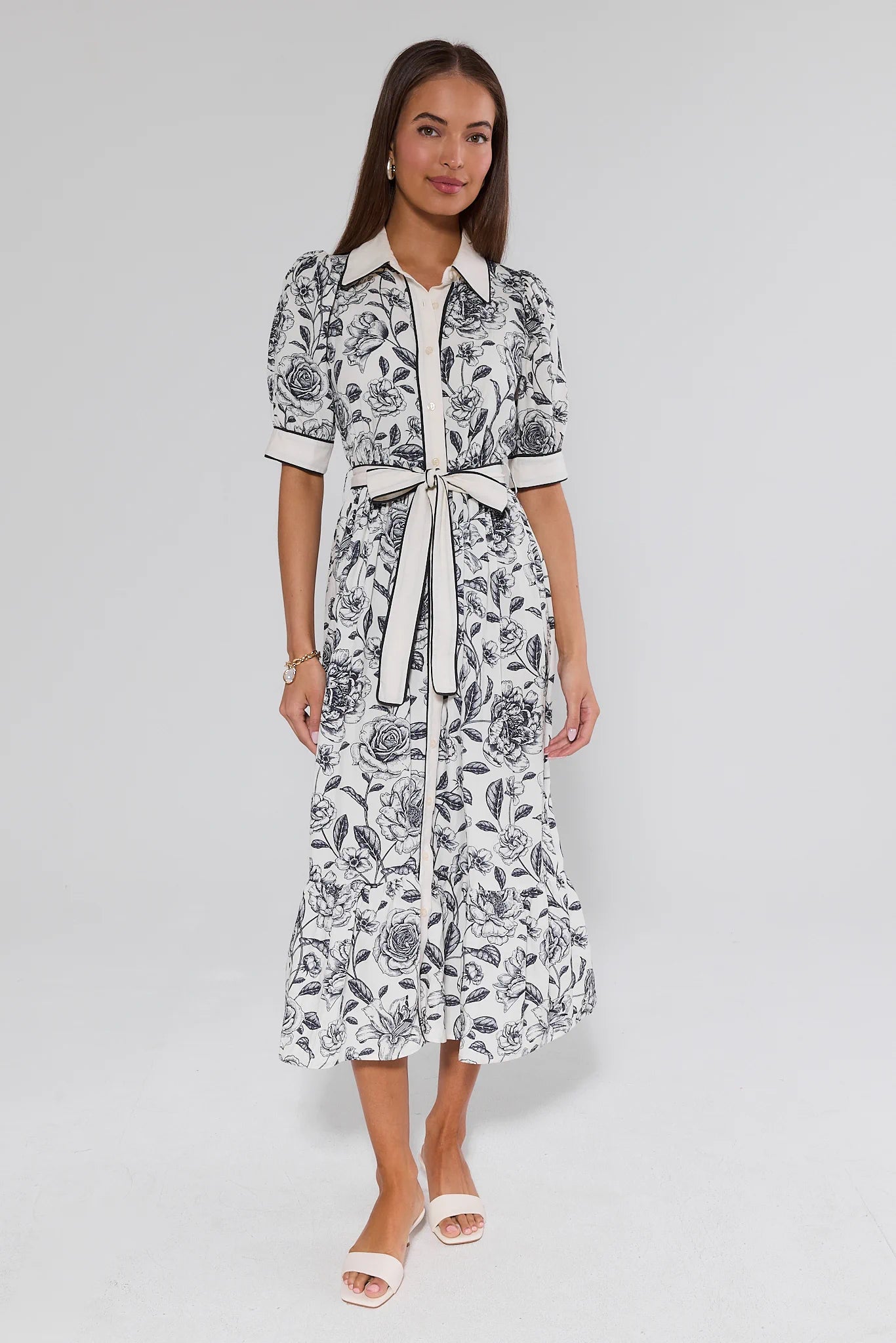 Woman wearing a black and white floral dress with a belt on a gray background