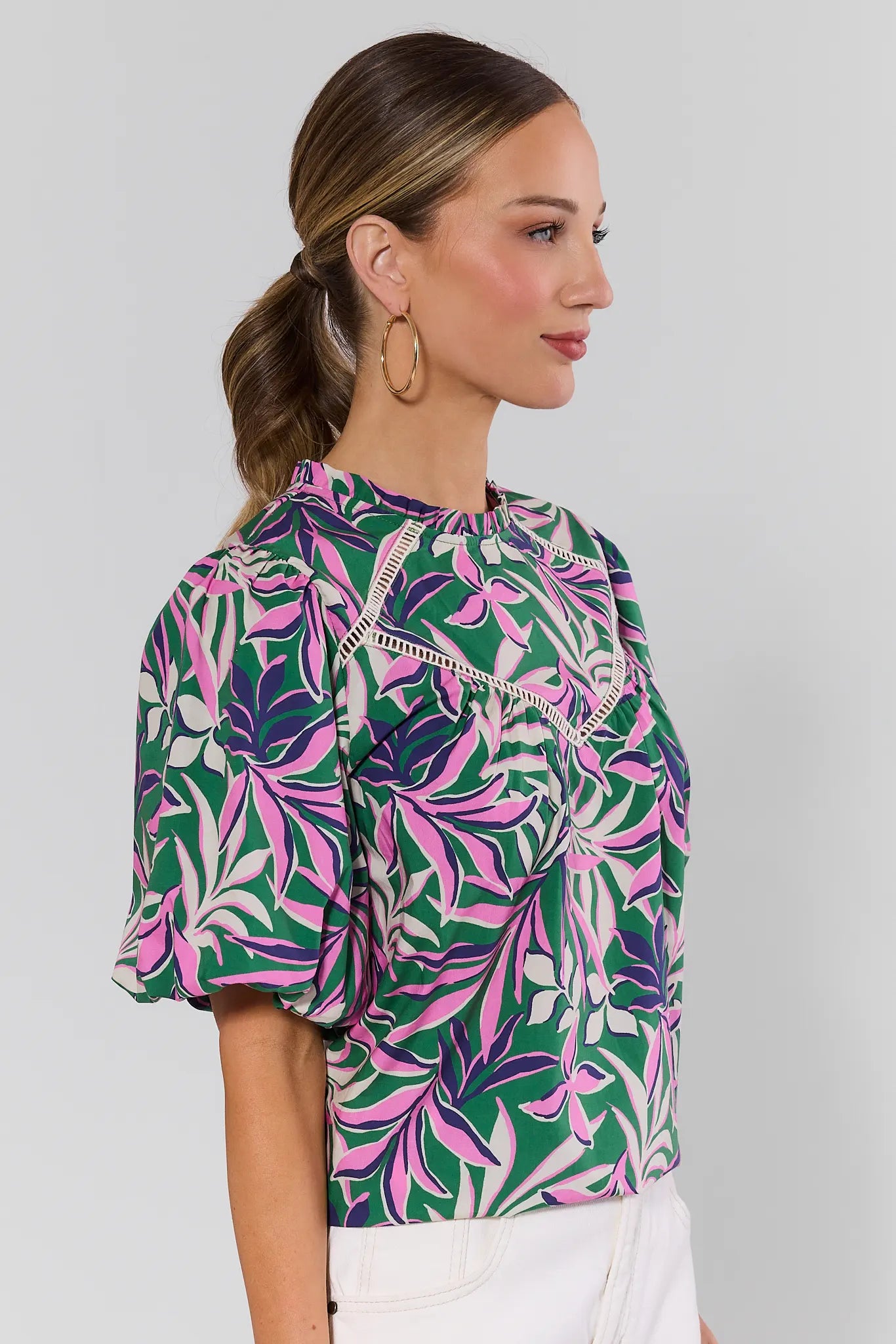 side shot Woman wearing a colorful leaf-patterned blouse against a gray background