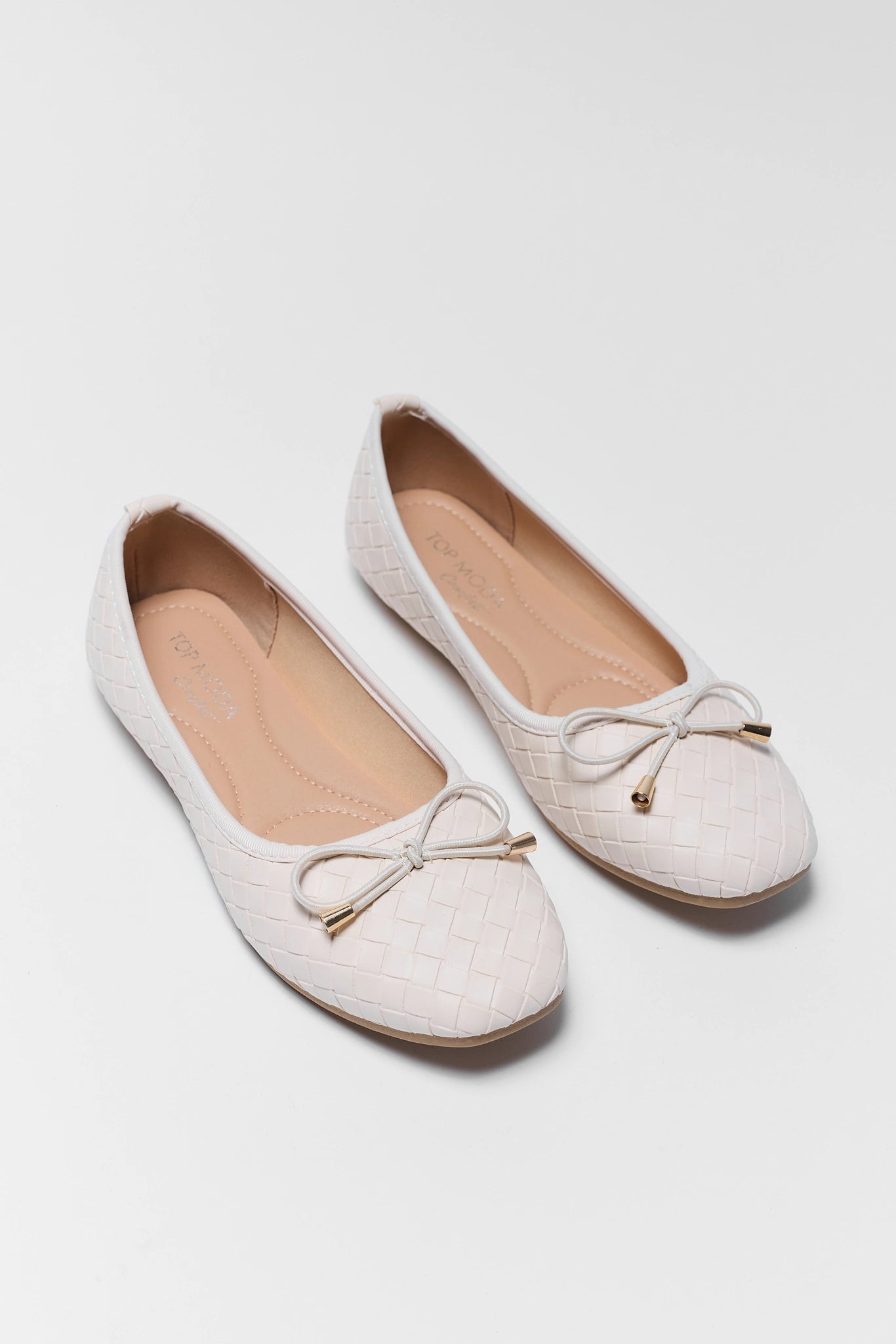 Pair of white flat shoes with bow details on a light background