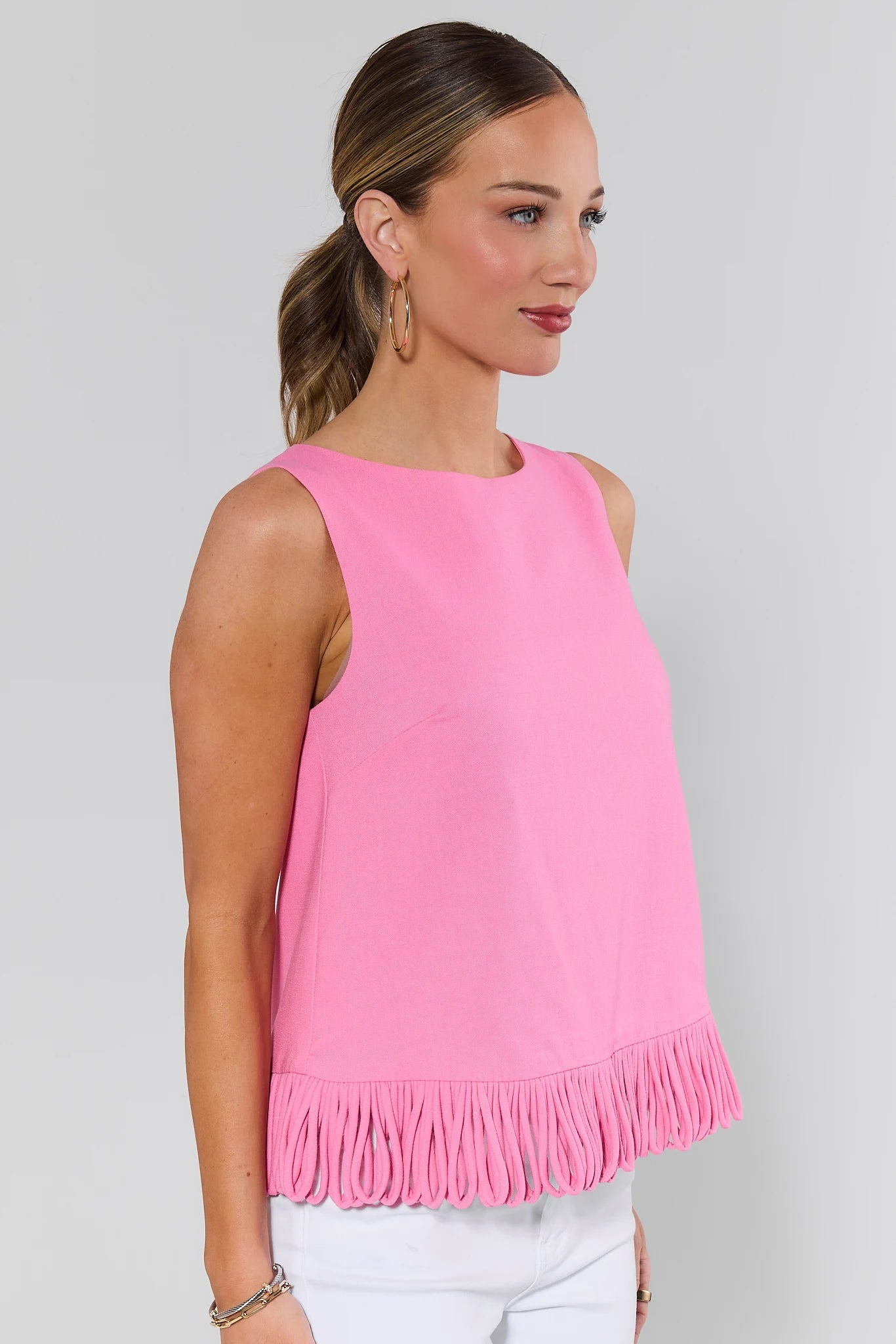 side shot Woman wearing a pink sleeveless top with fringe details on a gray background