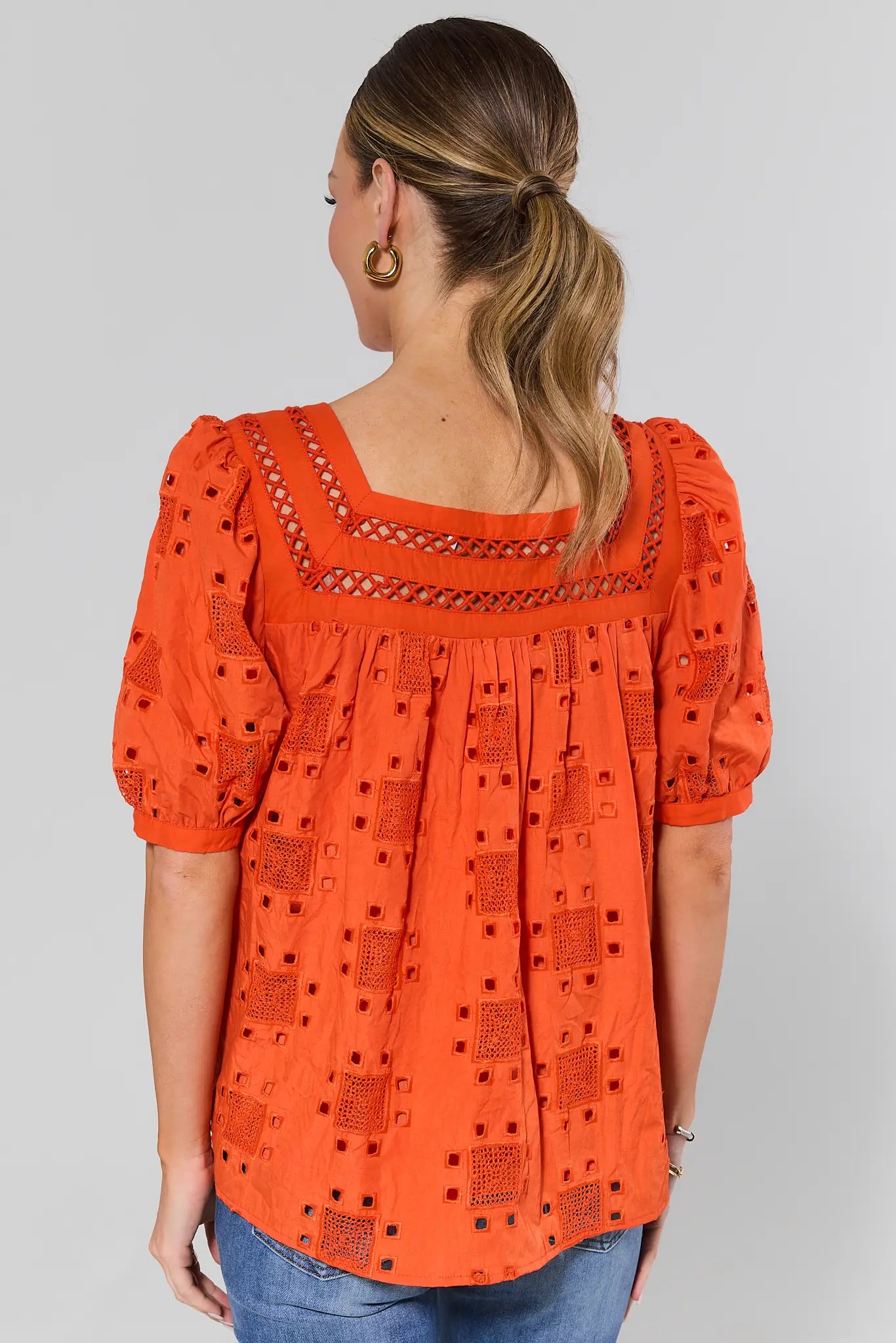 Woman standing wearing an orange blouse with a pattern on a gray background