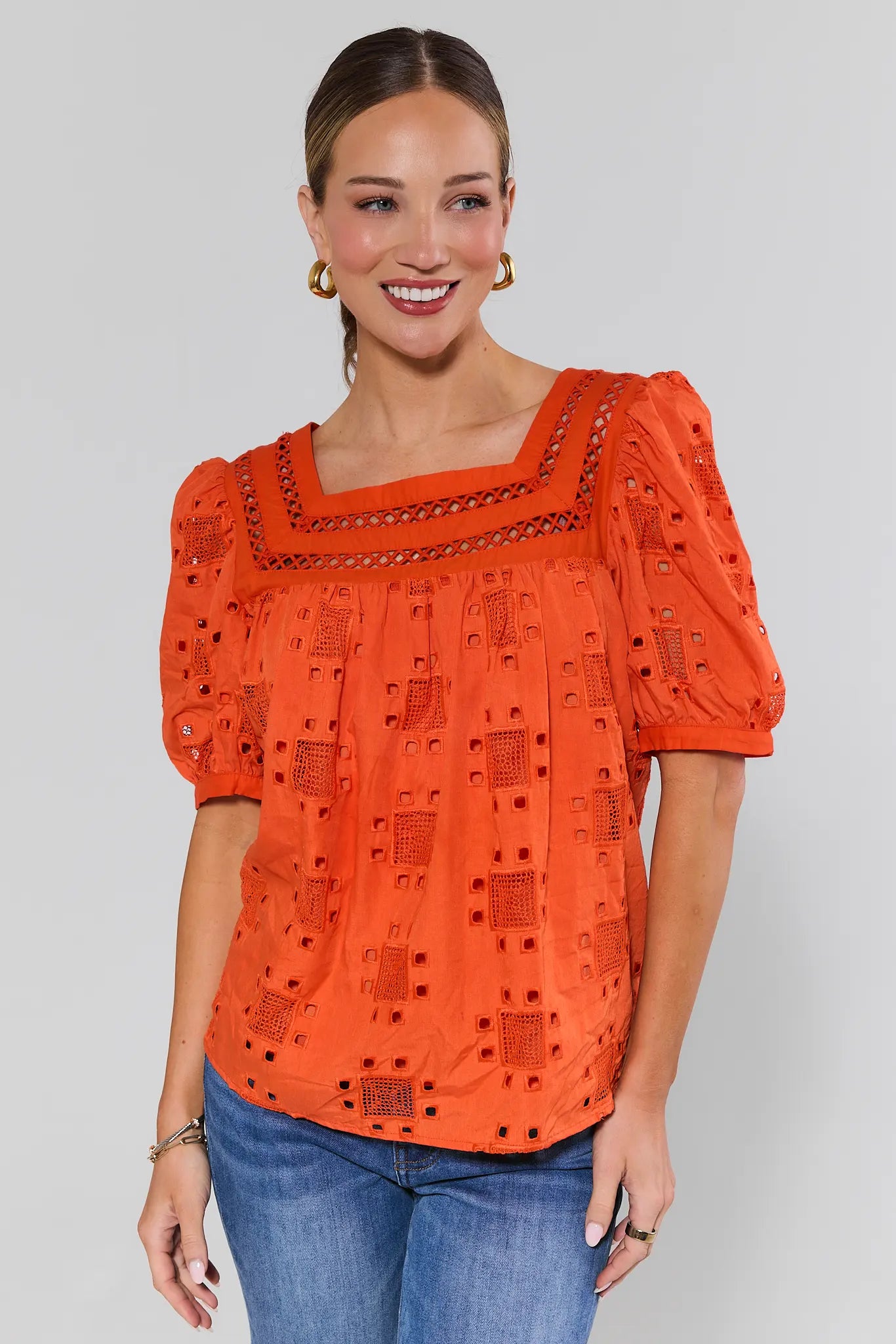 Woman wearing an orange ines blouse with intricate patterns on a plain background