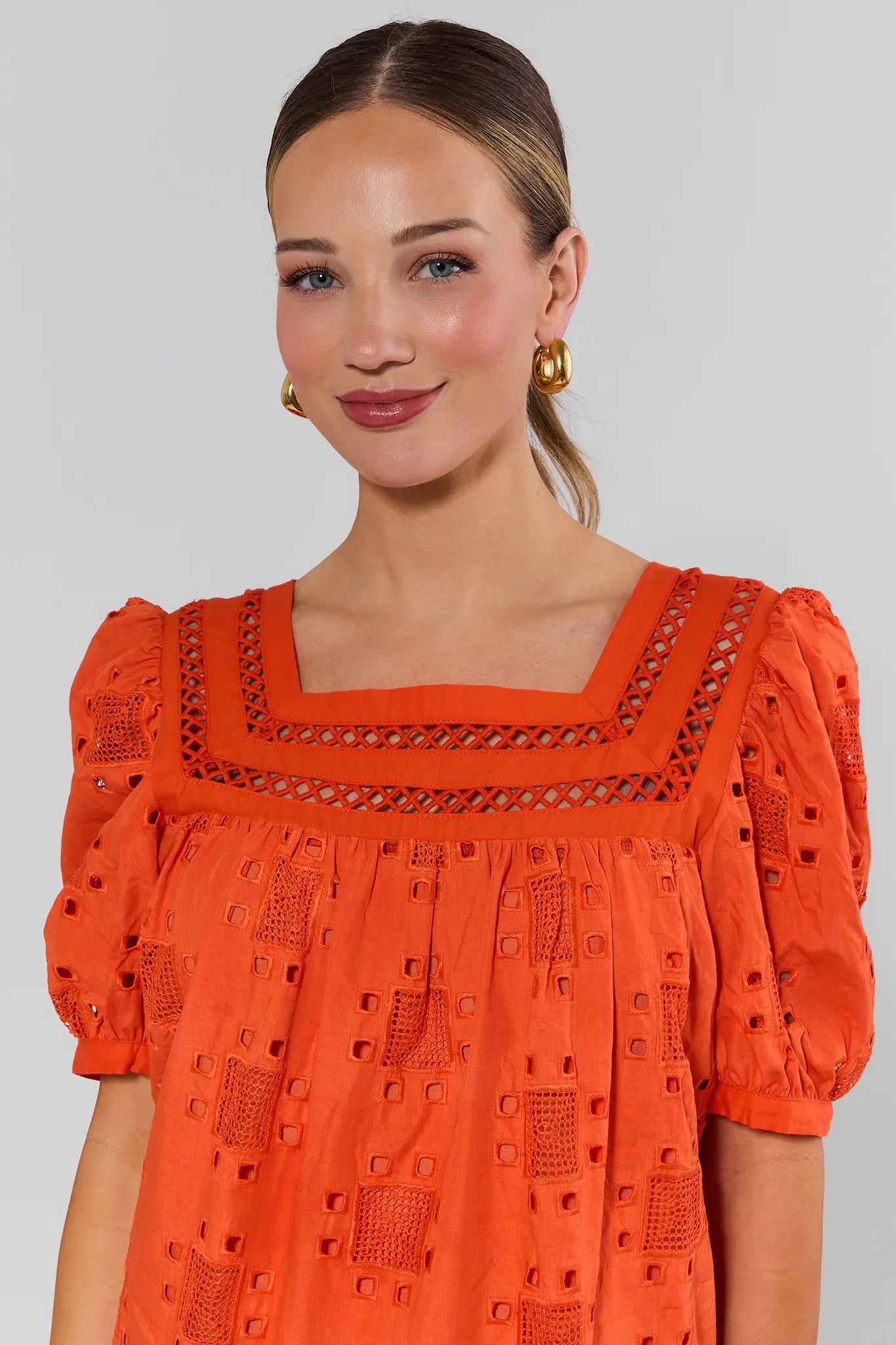 close up Woman wearing an orange dress with intricate details on a plain background