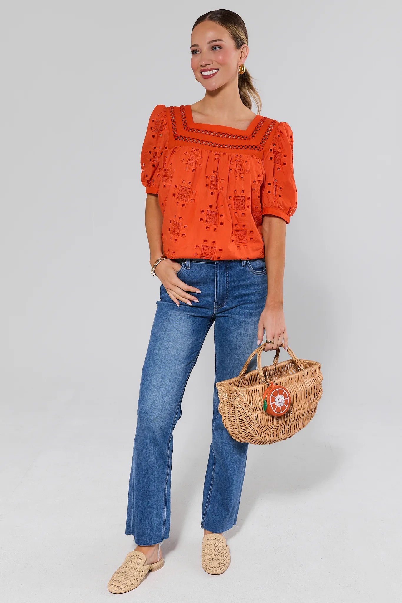 Woman wearing an orange blouse and blue jeans, holding a wicker bag on a white background