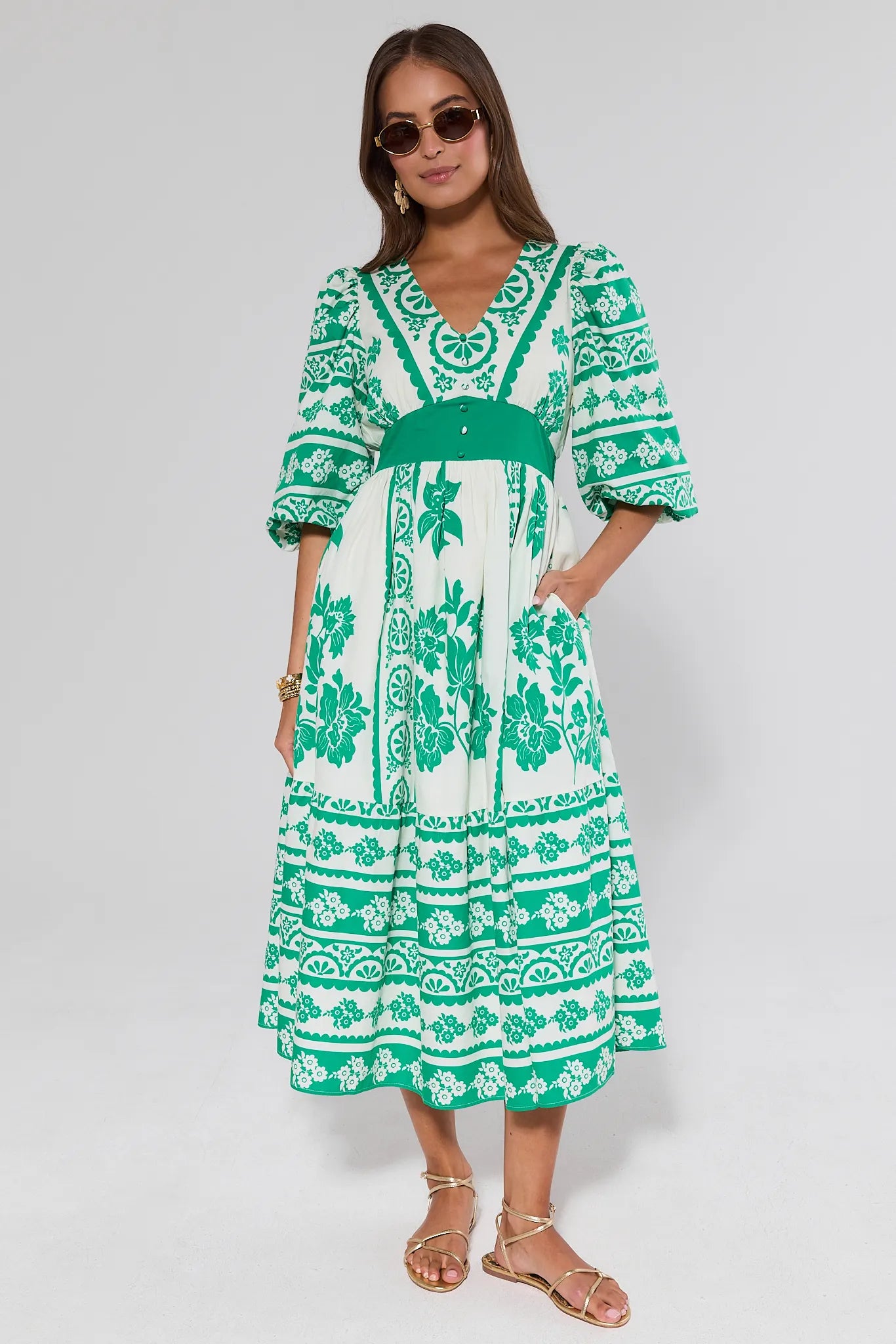 Woman wearing a green and white hadley patterned dress on a plain background