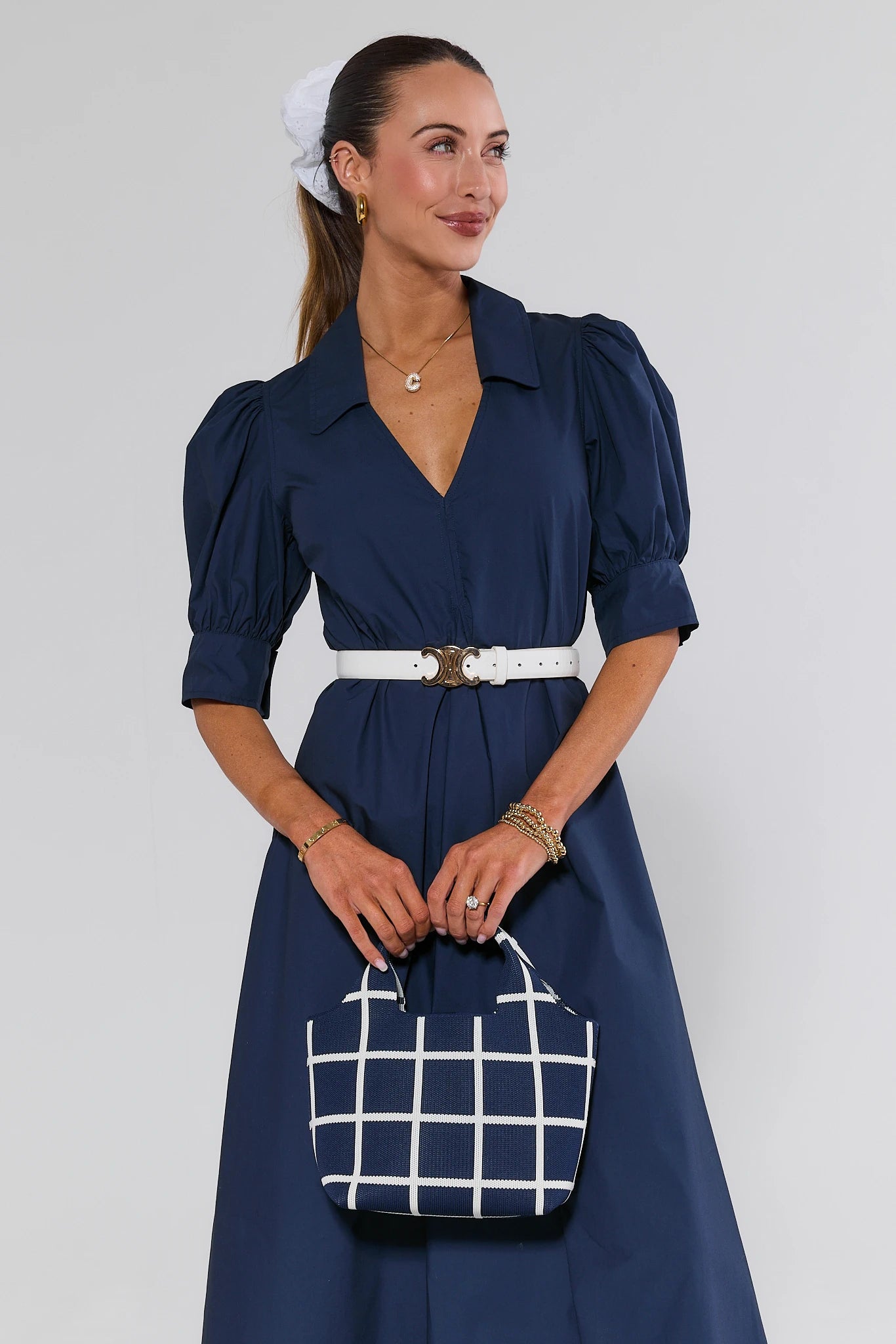 Woman in a navy dress holding a matching handbag against a white background